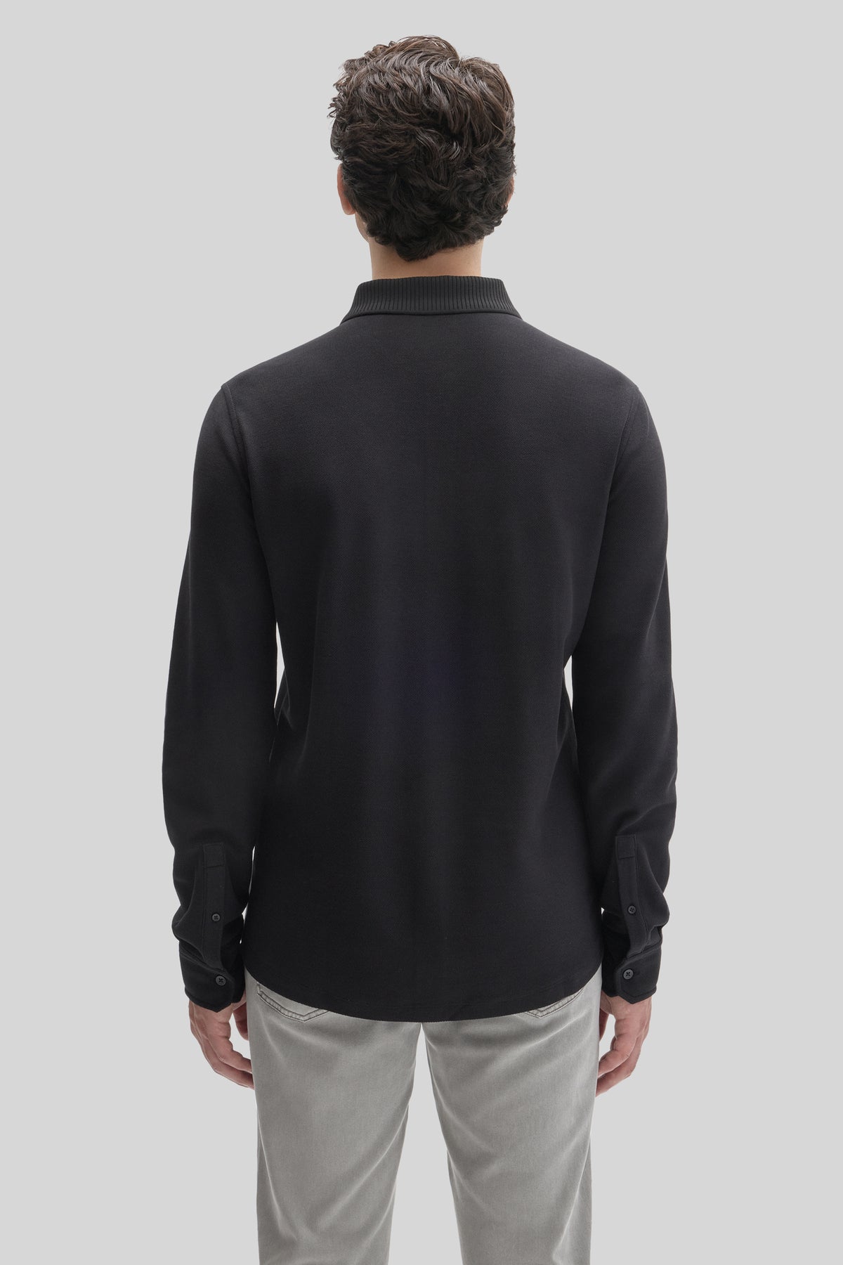Black long sleeve knit shirt with ribbed collar and button cuffs, shown from back on model wearing light gray pants.