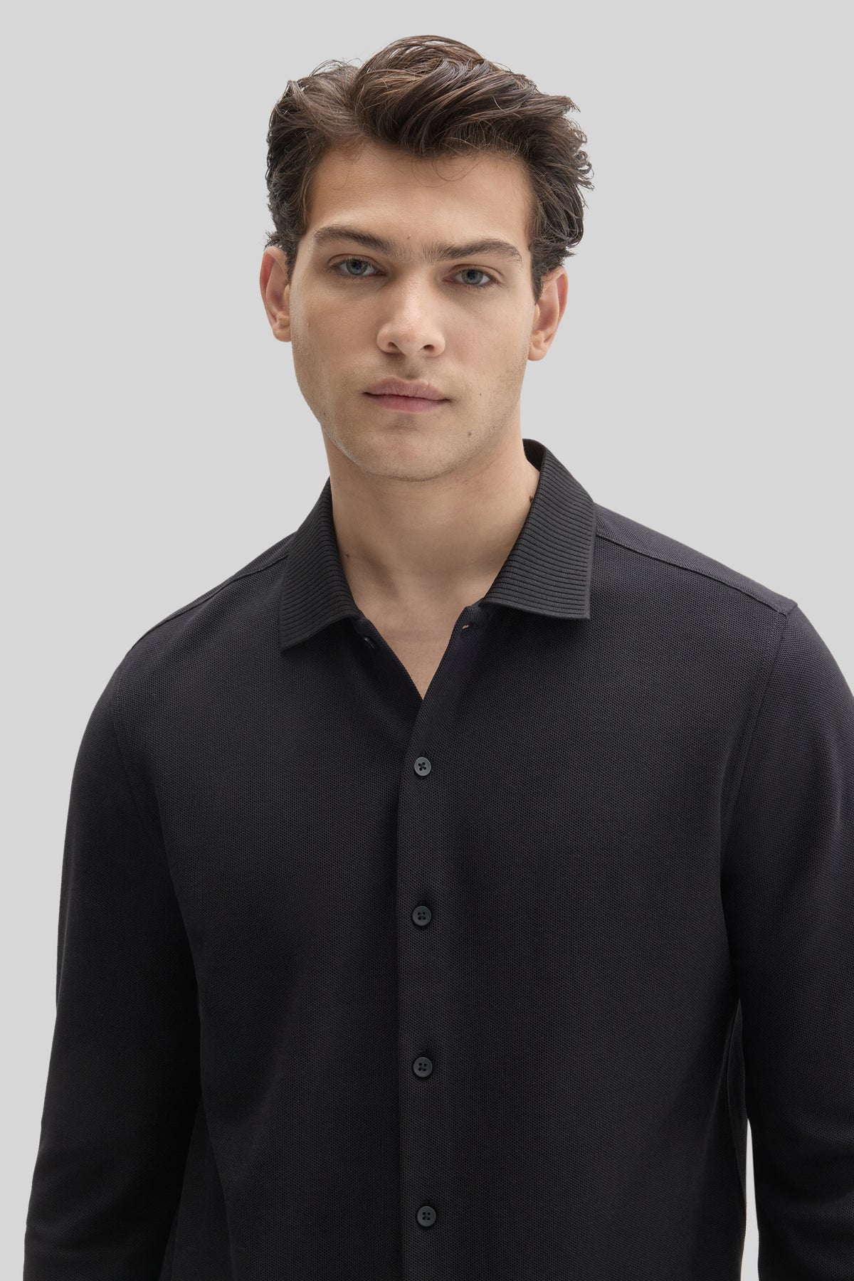 Man wearing black long sleeve knit shirt with ribbed texture and button front closure.