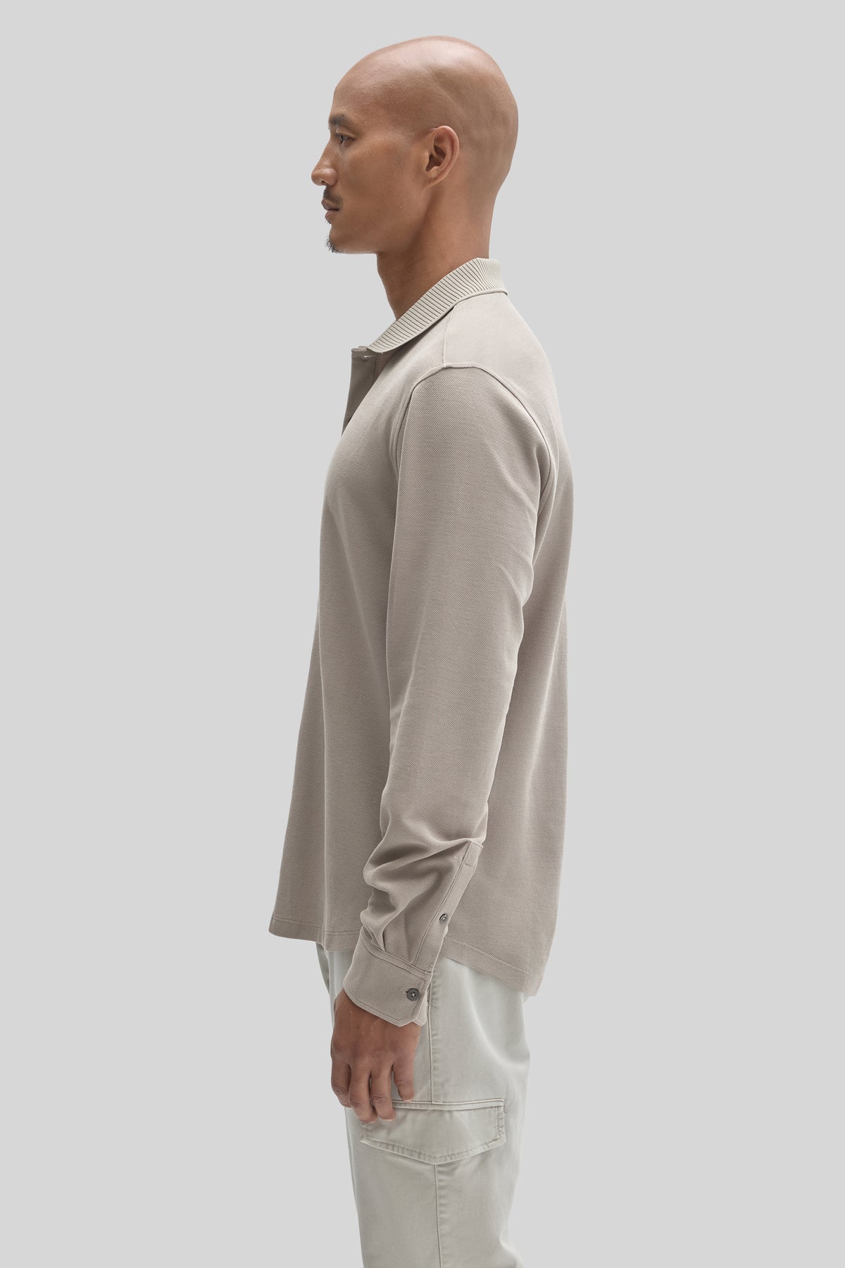 Cream-colored long sleeve knit shirt with ribbed collar and button cuffs, worn by model in side profile.