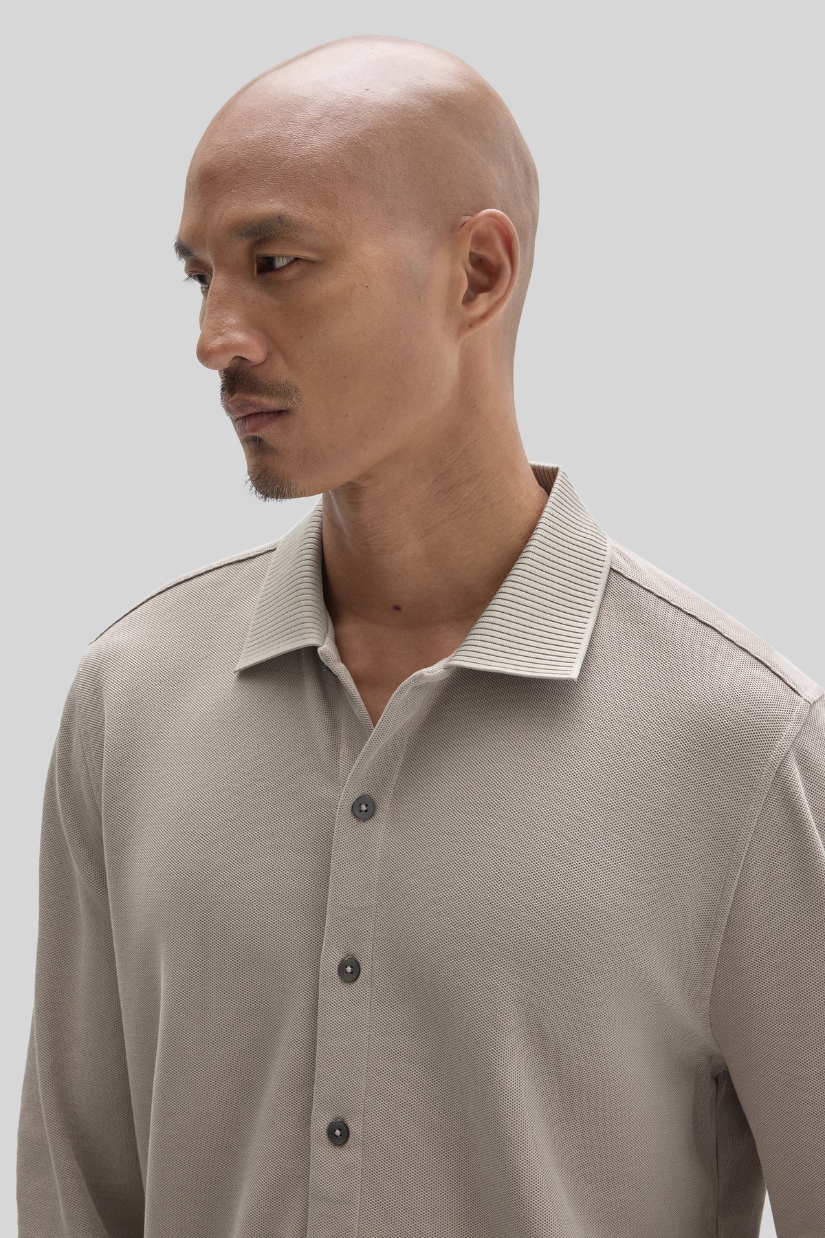 Beige long sleeve knit shirt with collar and button front, worn by man shown in profile view.