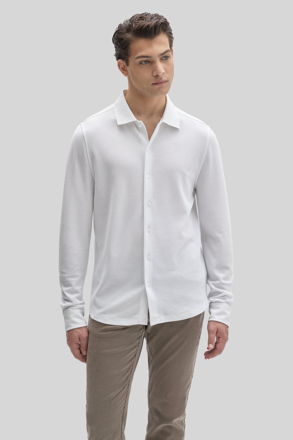 Man wearing white long sleeve knit shirt with collar and button front, paired with beige pants.