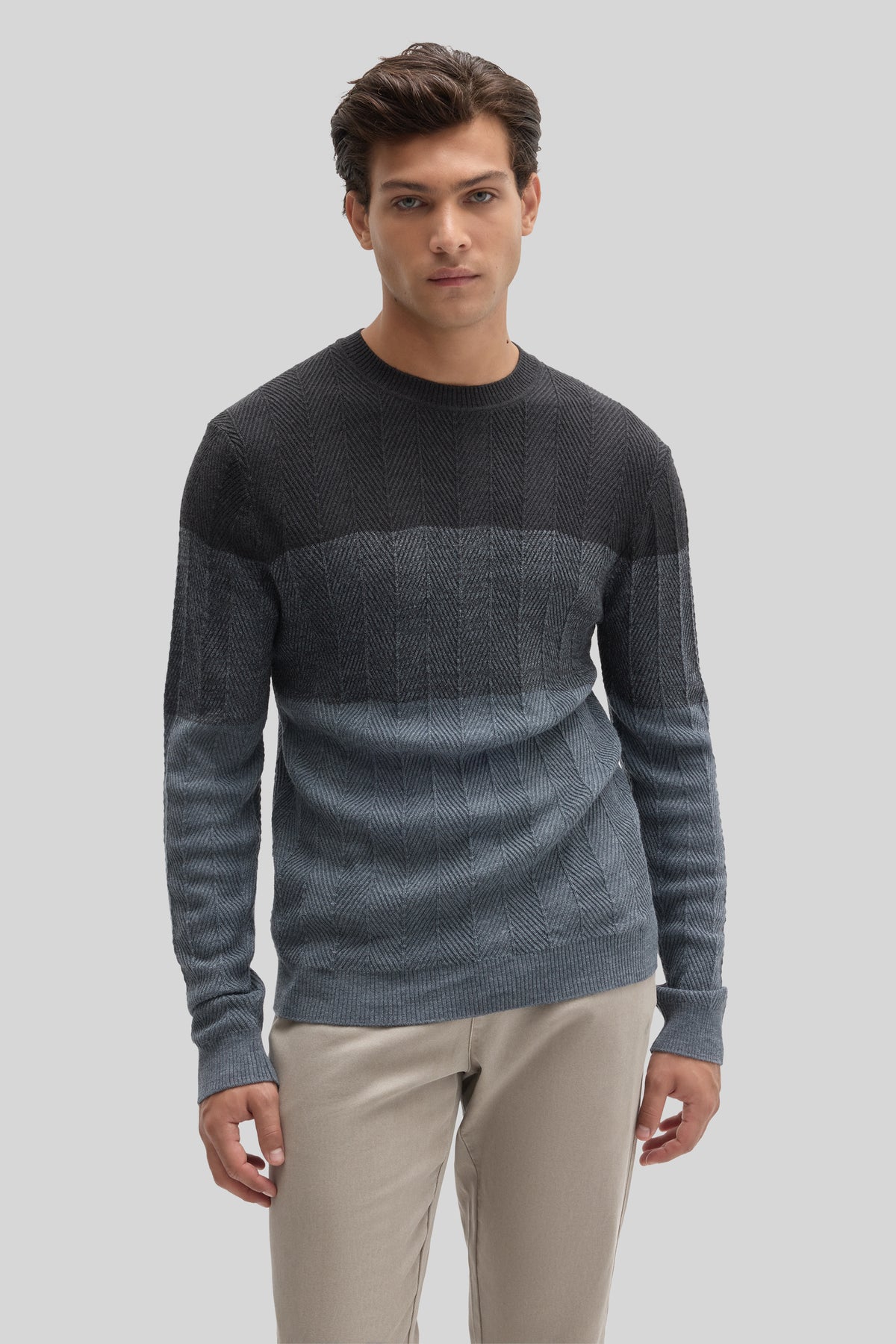 Charcoal herringbone crewneck sweater with color-block horizontal stripes worn with cream pants.