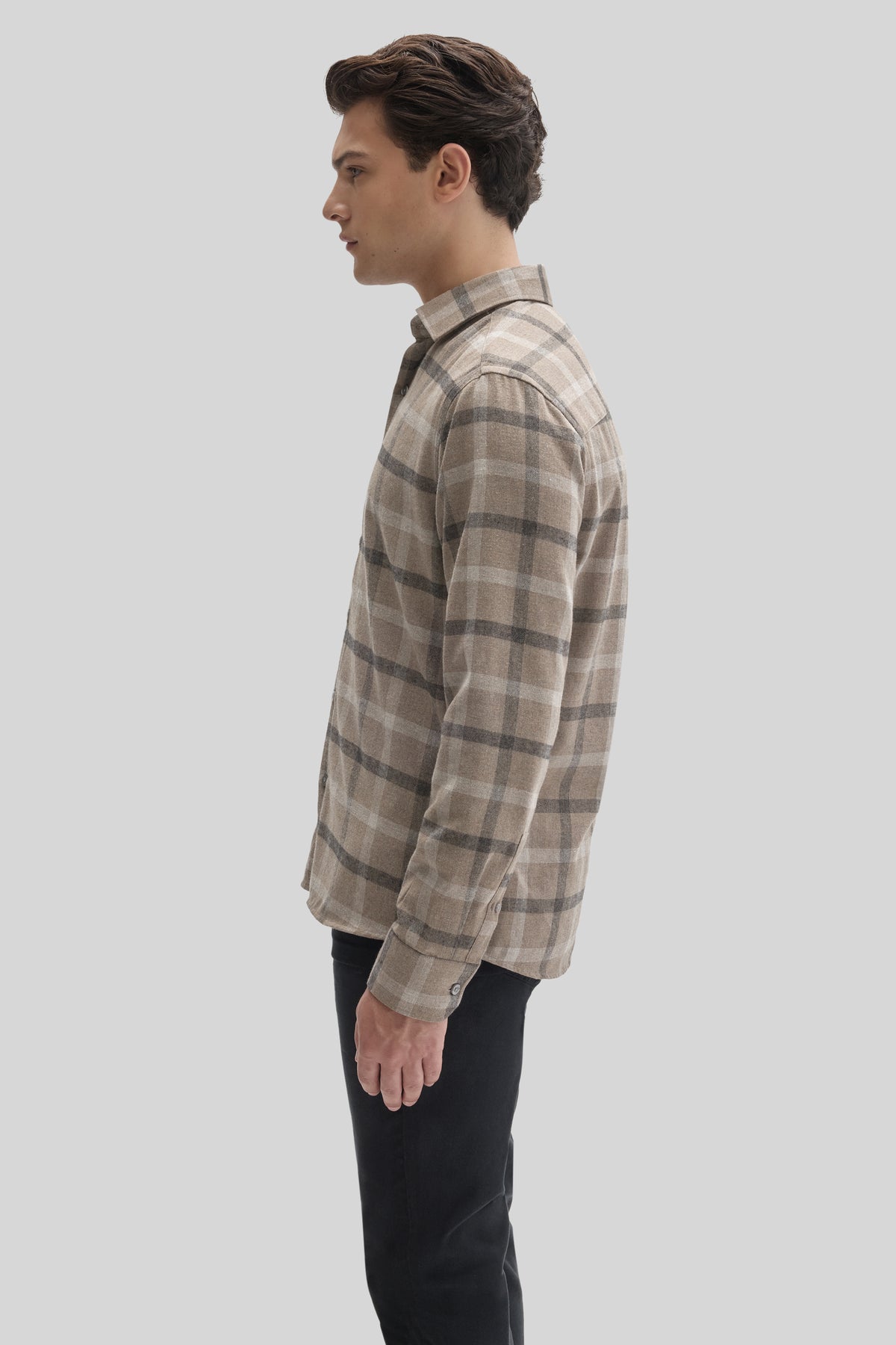 Man wearing a tan and gray plaid flannel shirt with a collared neckline over black pants, shown in profile.