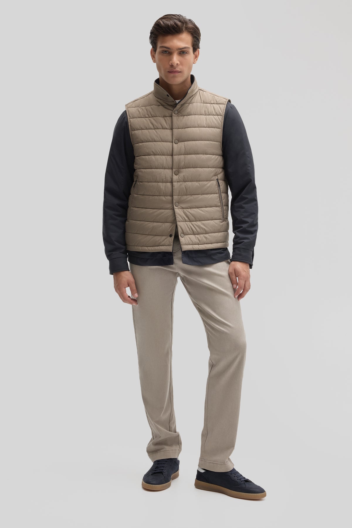 Man wearing beige quilted vest over black long-sleeve shirt with khaki pants.