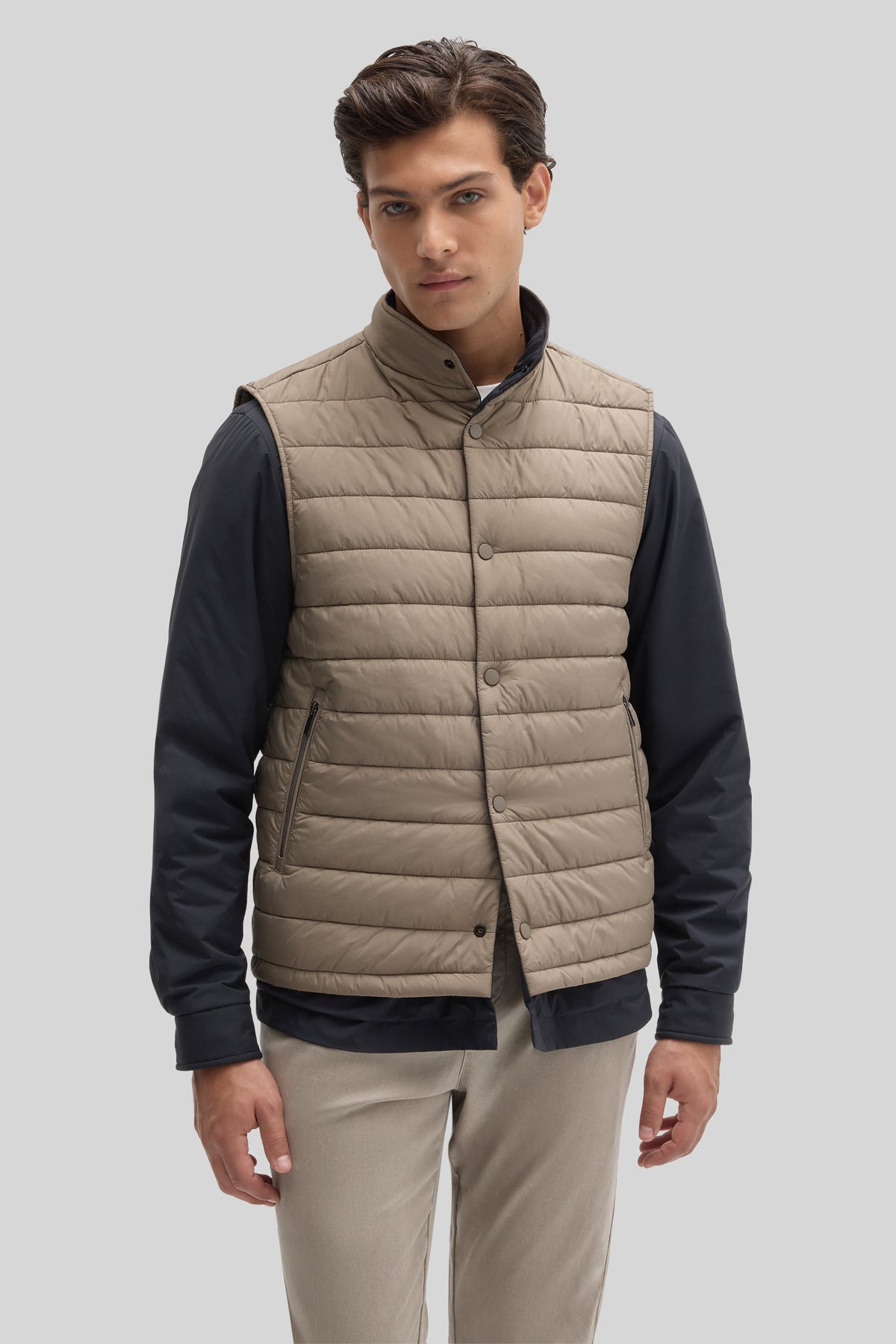Beige quilted vest with snap closure worn over navy long-sleeve shirt, paired with cream pants.