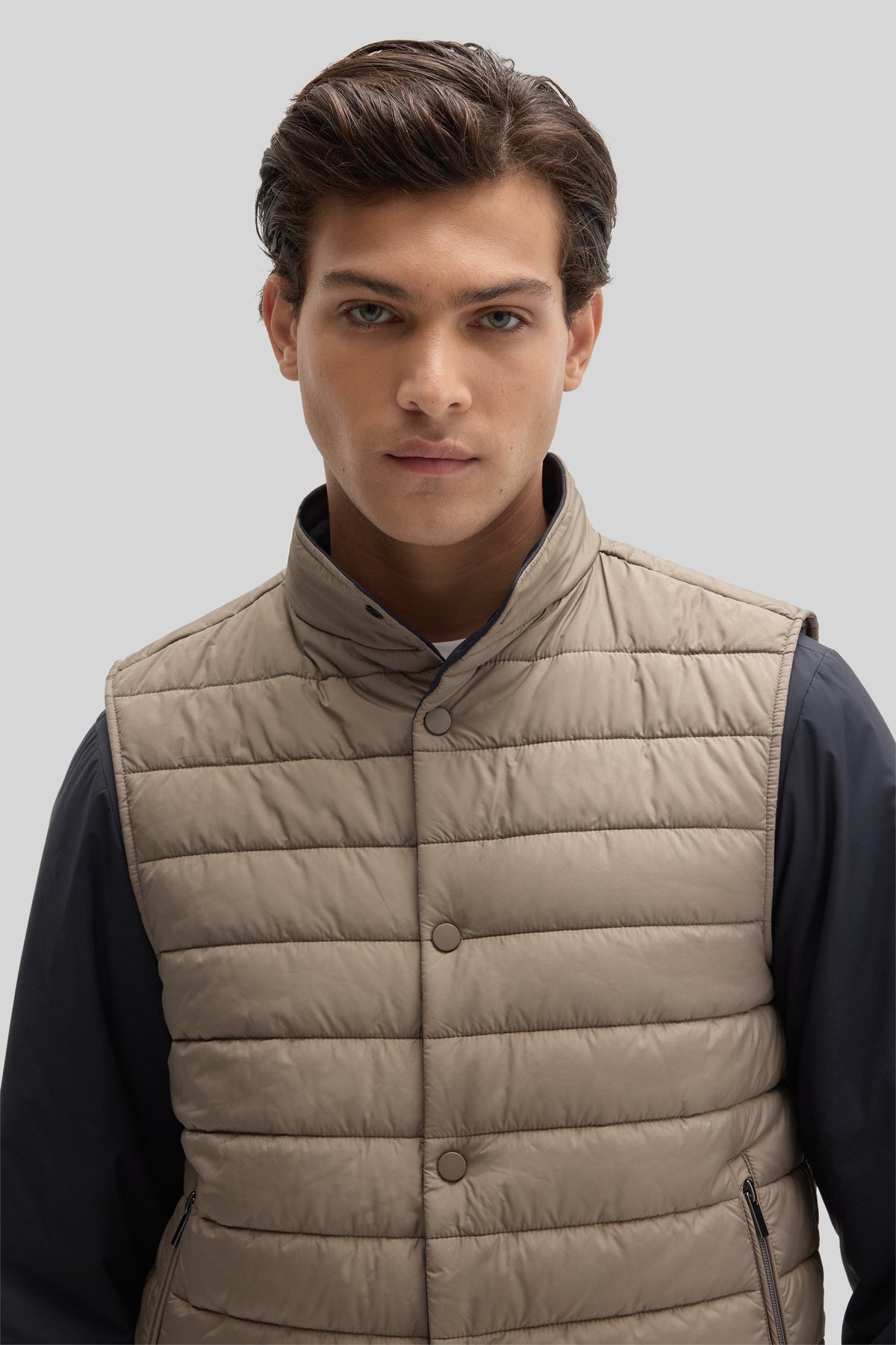 Man wearing beige quilted puffer vest with snap closures over dark navy long-sleeve shirt.