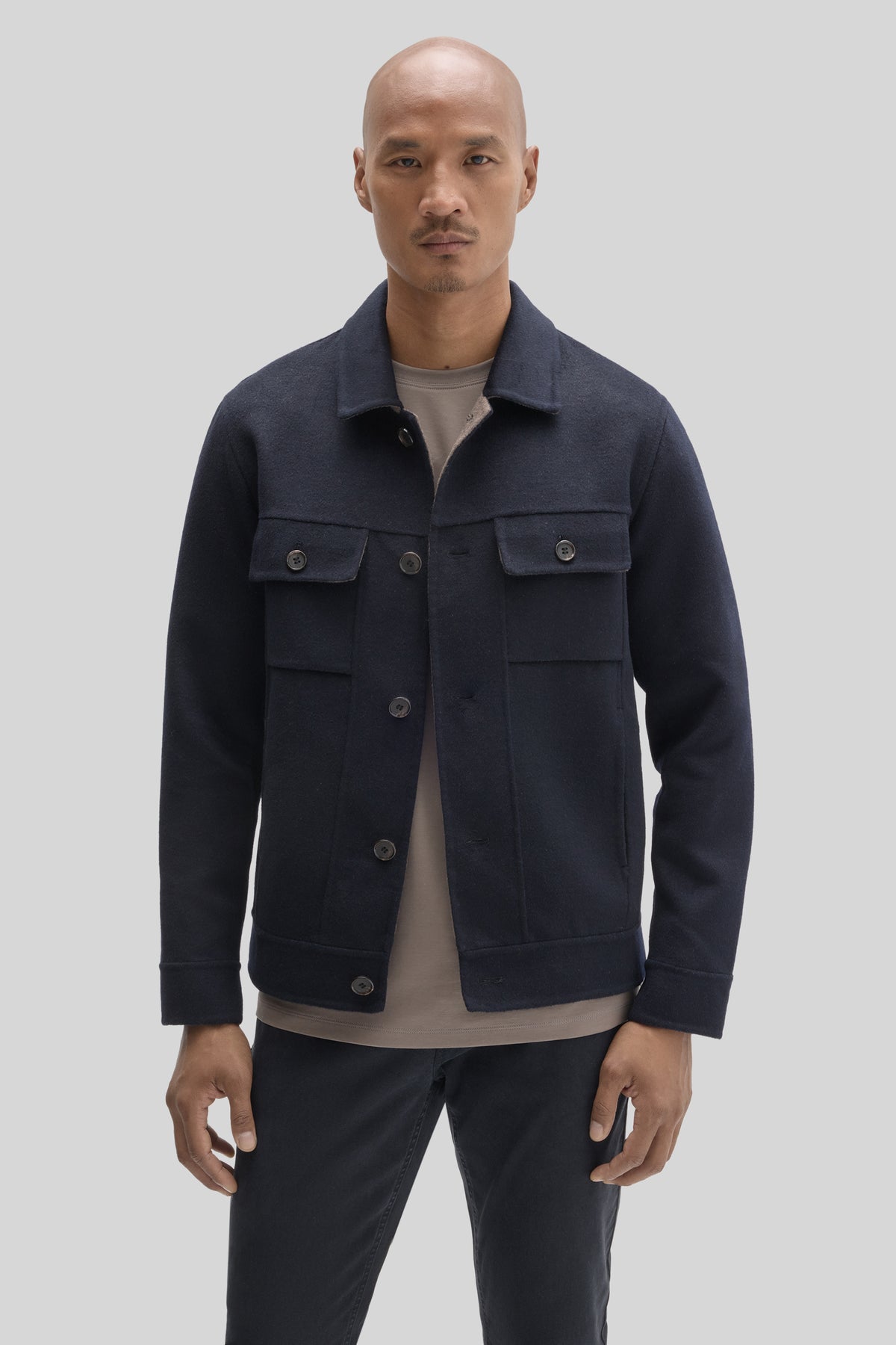 Navy buttoned jacket with chest pockets and metal buttons on model wearing beige shirt.