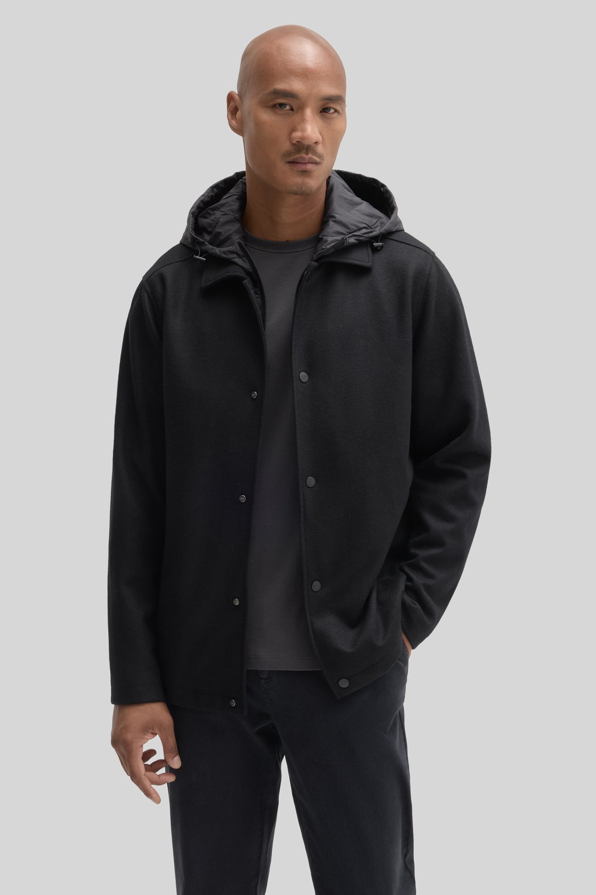 Black car coat with button front, hood, and quilted lining worn over dark shirt and trousers.
