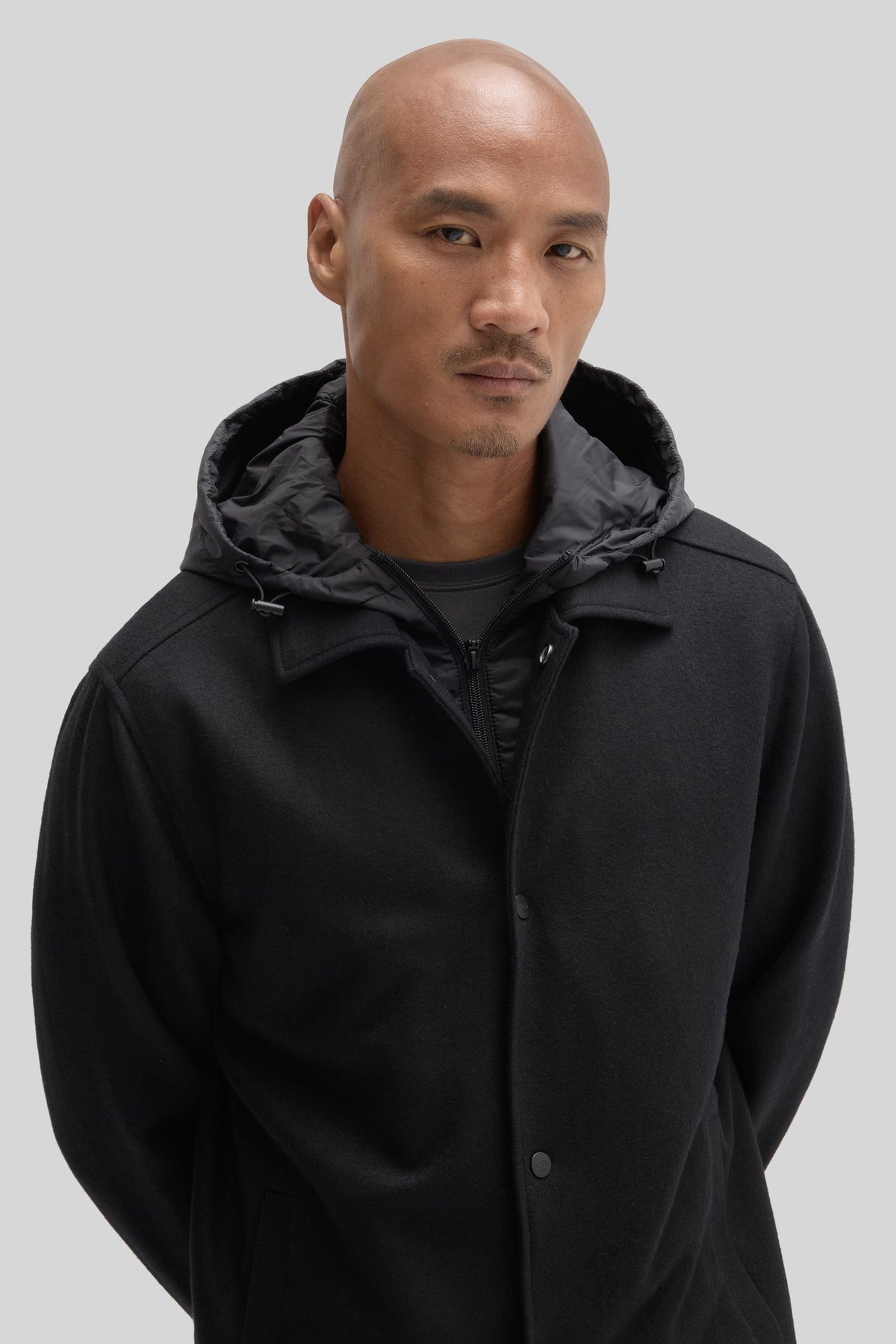 Black car coat with quilted hood lining and button front closure worn by a man.