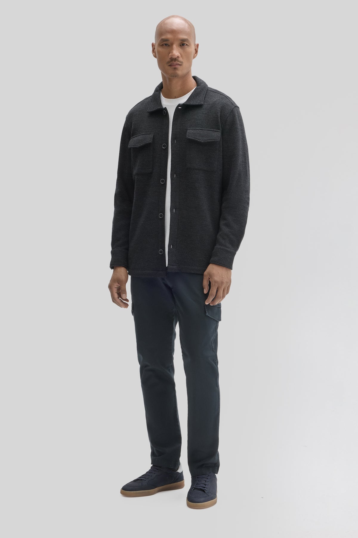 Charcoal overshirt with chest pockets and button front worn with white tee, dark cargo pants, and navy sneakers.