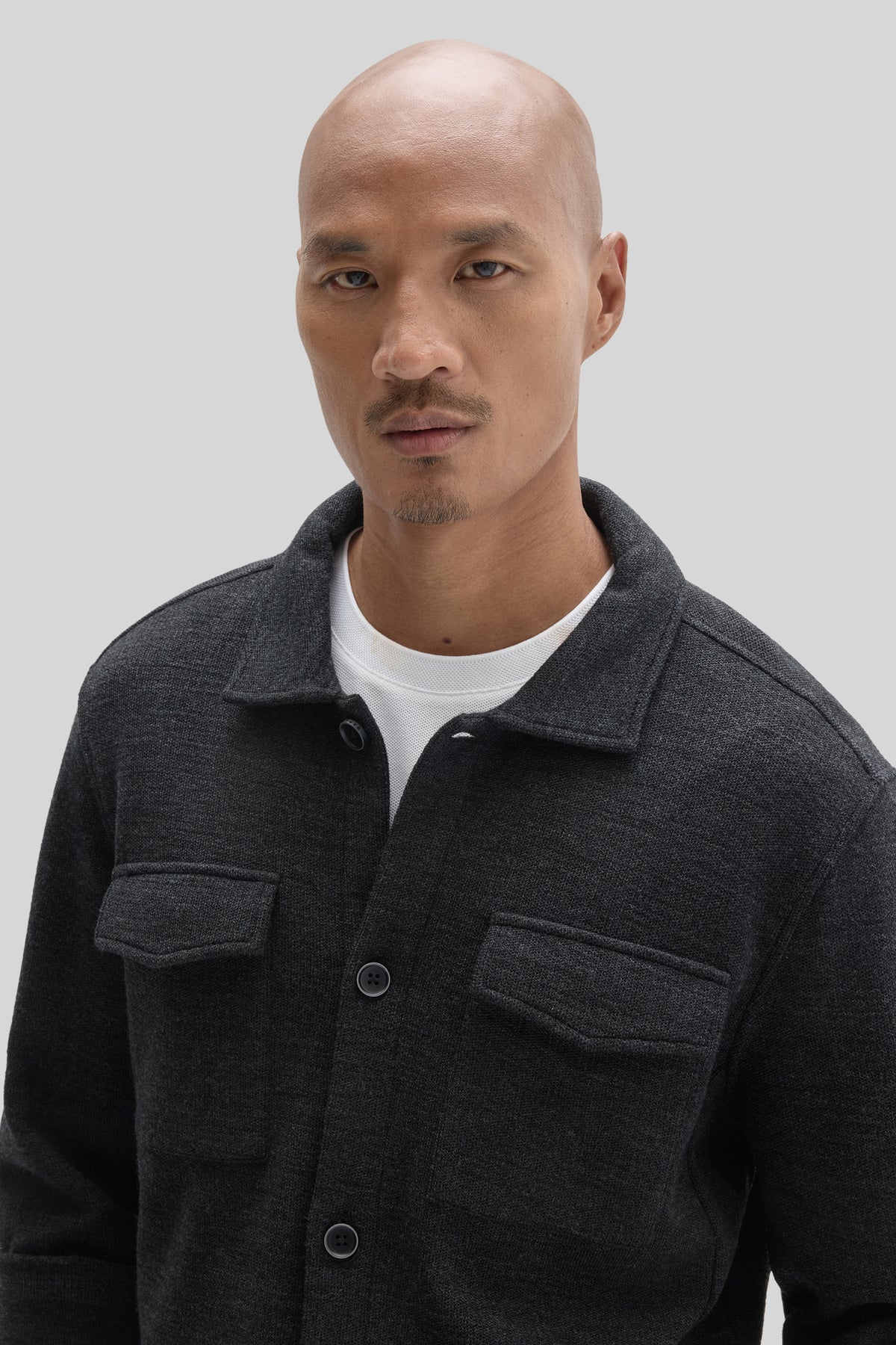 Charcoal gray overshirt with collared neckline, button front closure, and chest pockets worn over white t-shirt.