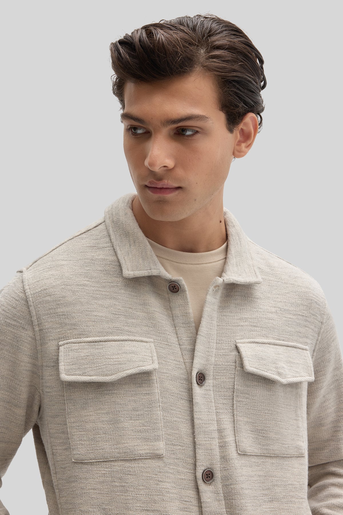 Cream-colored overshirt with textured knit fabric, collar, button front, and two chest pockets worn over a light t-shirt.