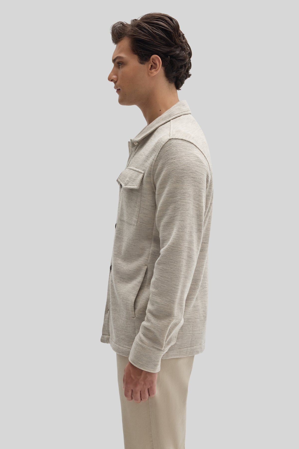 Beige overshirt with textured fabric, collar, front button closure, and chest pocket on model in side profile.