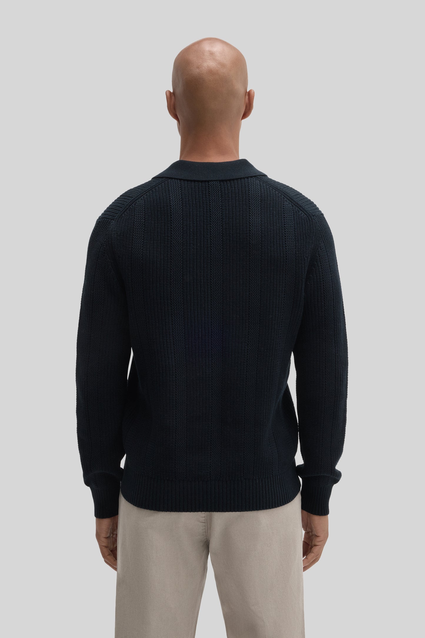 Black knit sweater polo with collar, worn with beige trousers, shown from back view.