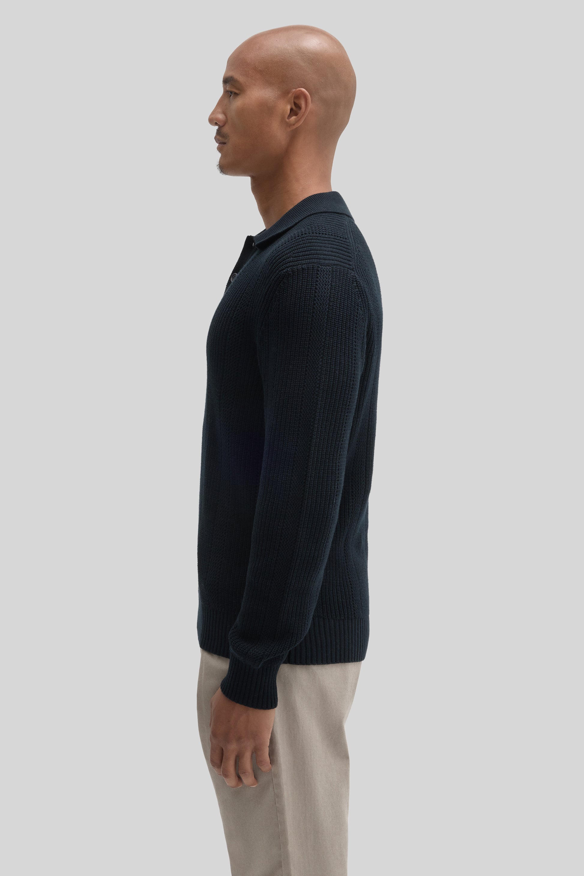 Man wearing dark navy ribbed sweater polo with collar and beige pants, shown in profile view.