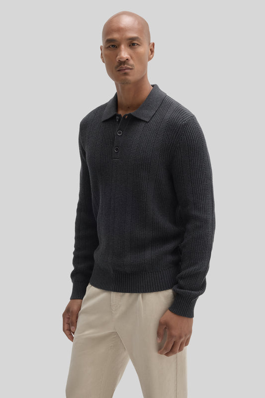Man wearing dark gray ribbed sweater polo with collar and button front, paired with cream-colored pants.