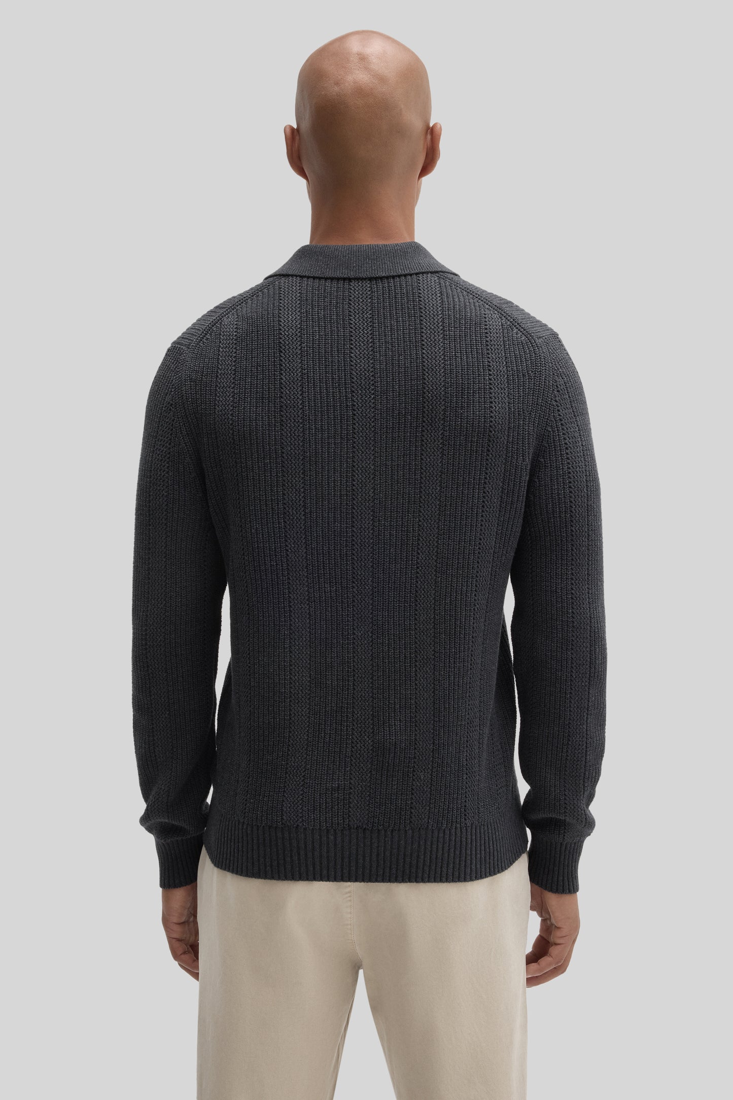 Man wearing dark gray ribbed knit sweater polo with collared neckline, viewed from back.