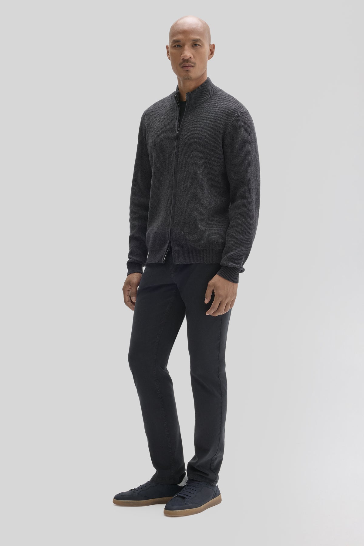 Man wearing charcoal gray full-zip mock neck sweater with ribbed knit texture and black pants.