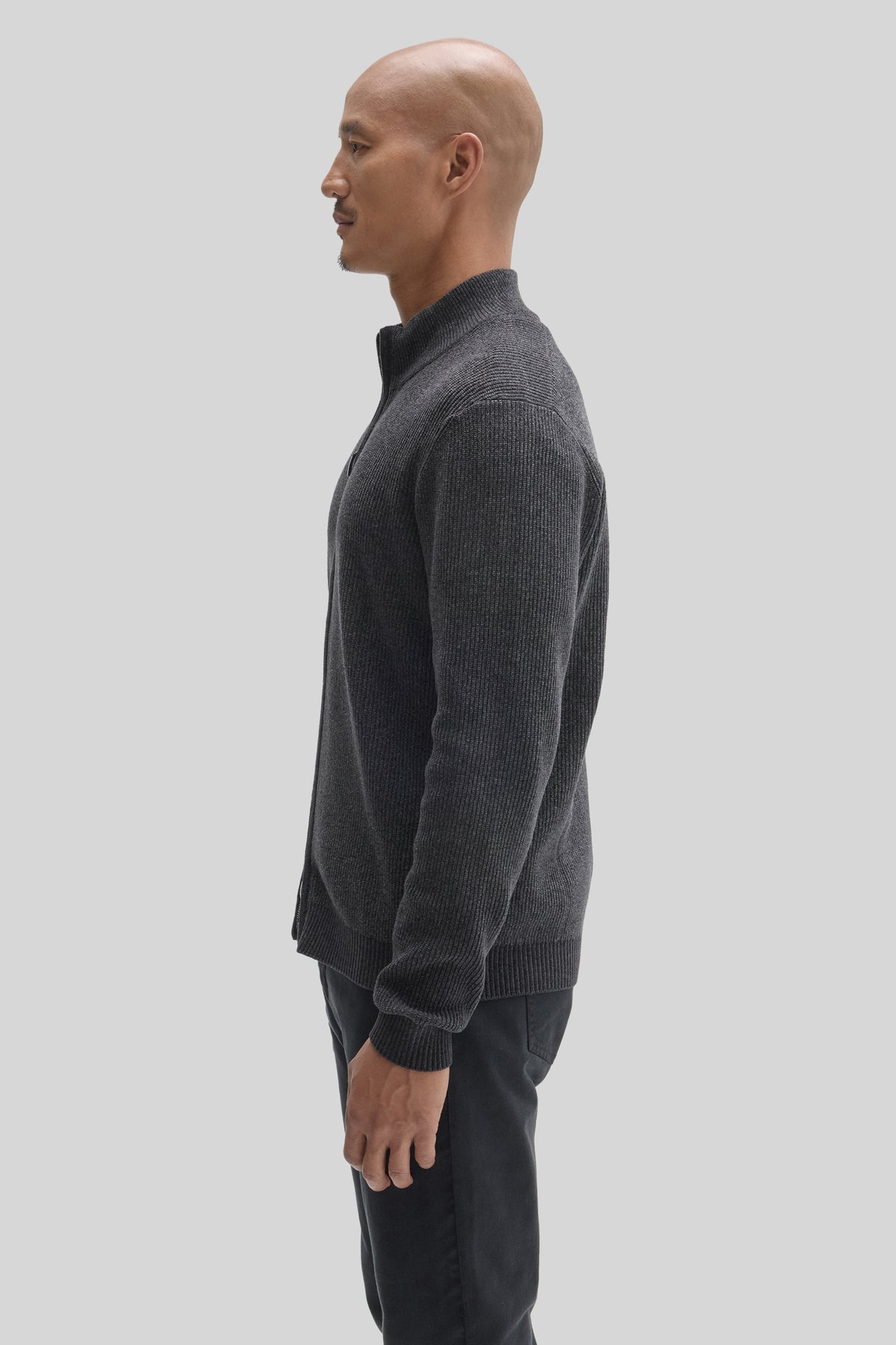 Charcoal ribbed full-zip mock neck sweater worn with black pants, shown from side profile.