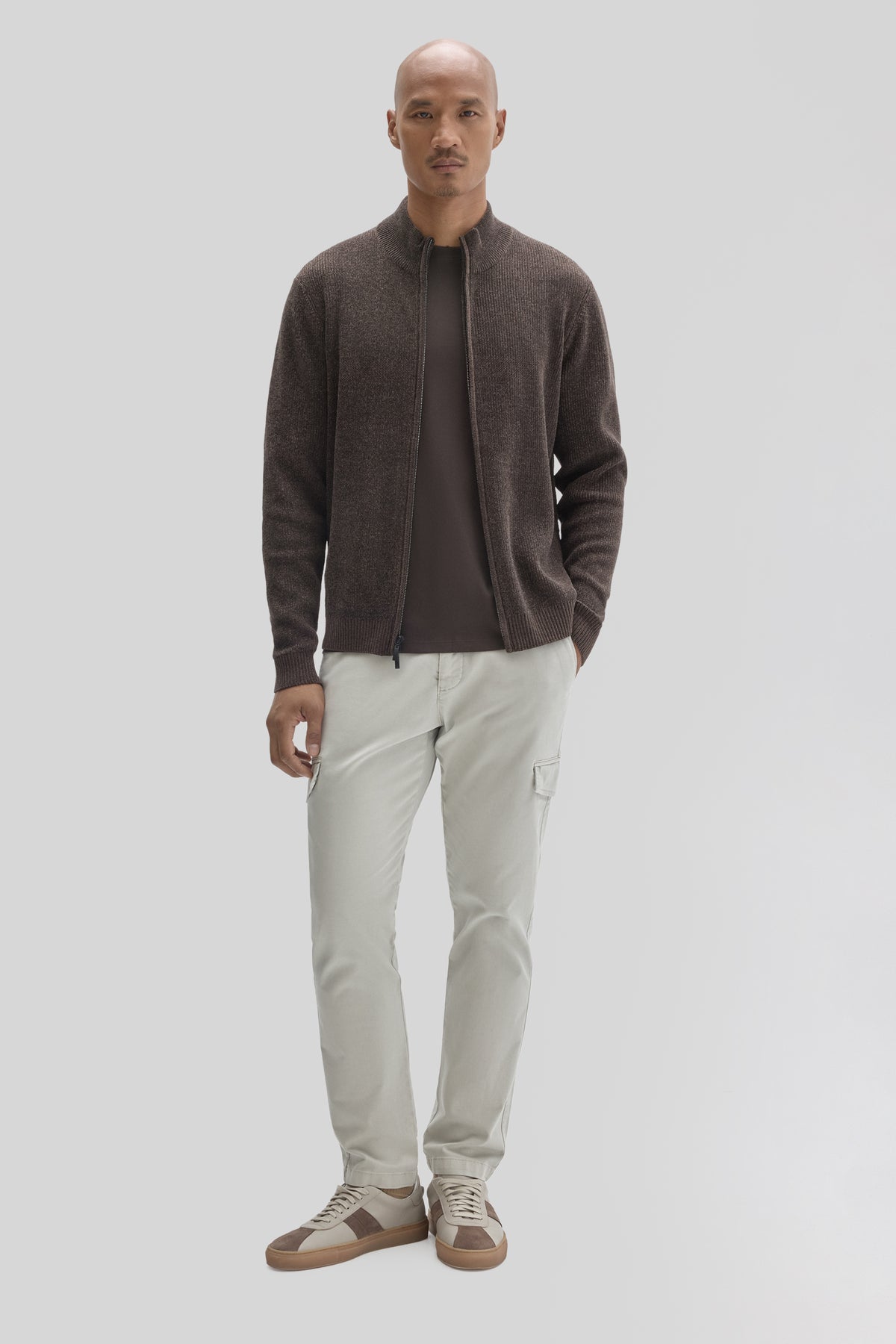 Man wearing charcoal mock neck full zip sweater over dark shirt, cream cargo pants, and tan sneakers.