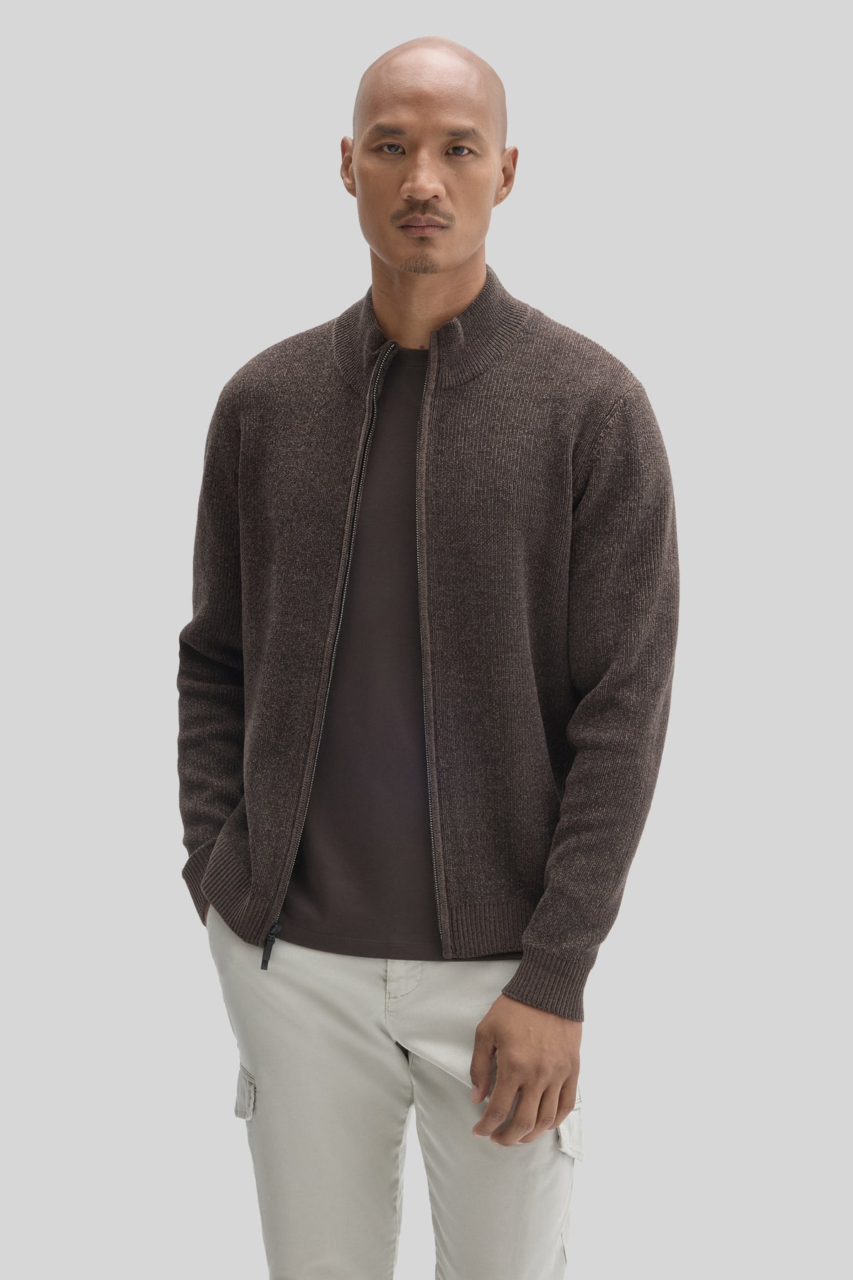 Man wearing charcoal mock neck full zip sweater over black shirt with cream cargo pants.