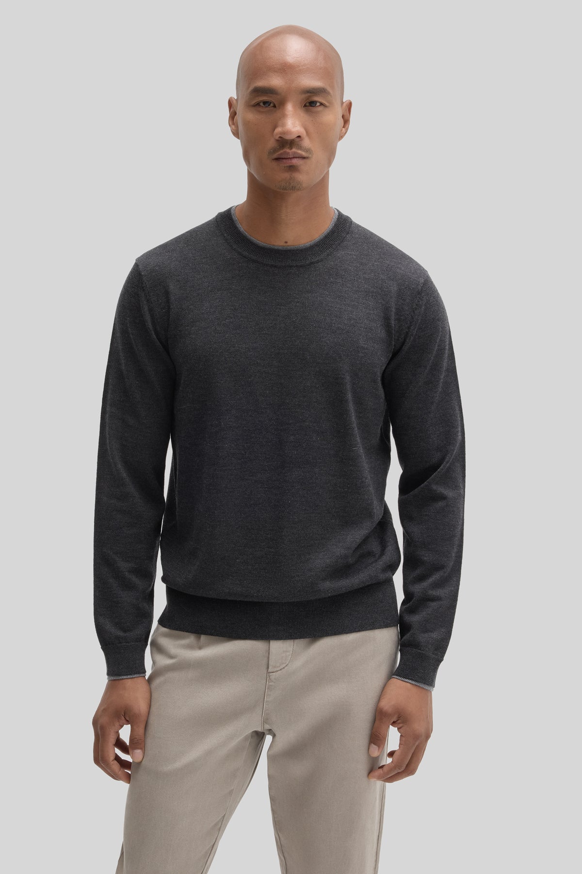 Charcoal crewneck sweater with ribbed cuffs and hem worn with beige pants.
