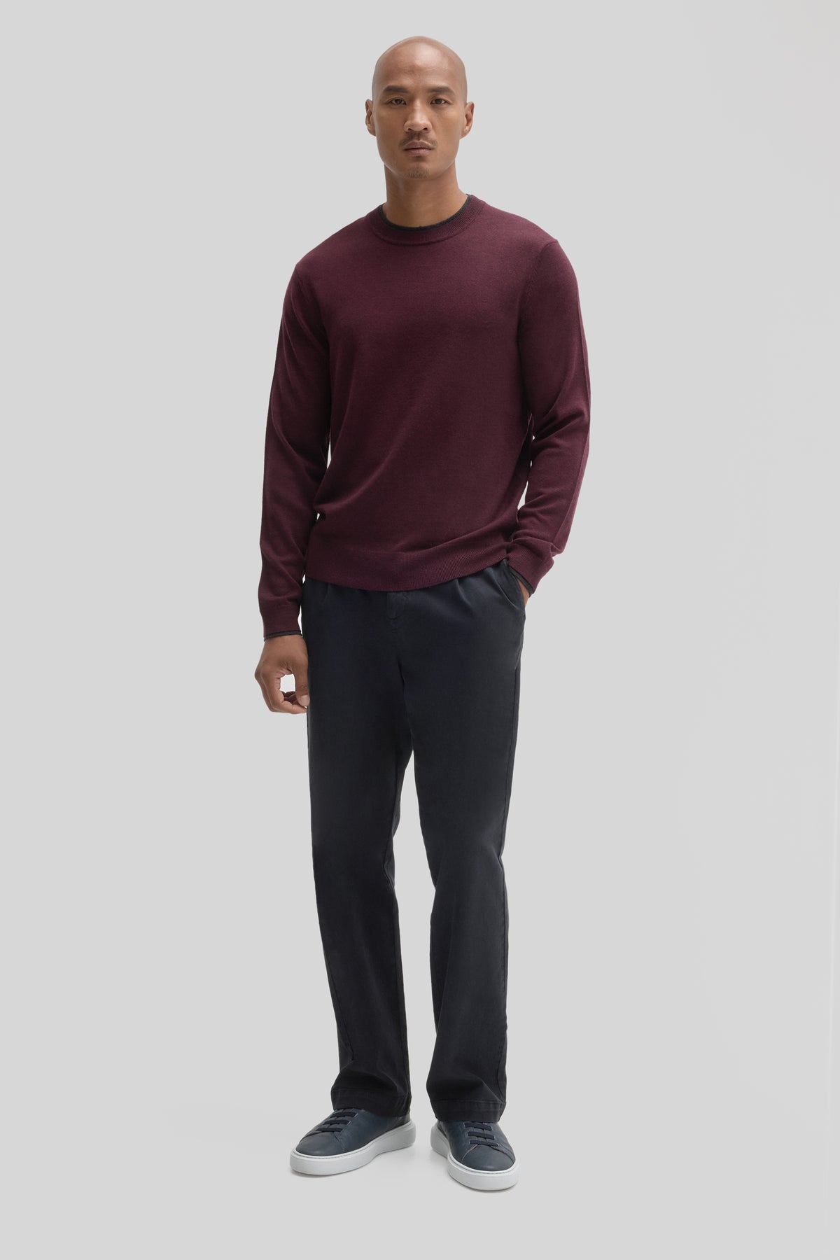 Man wearing burgundy crewneck sweater with black pants and navy sneakers.