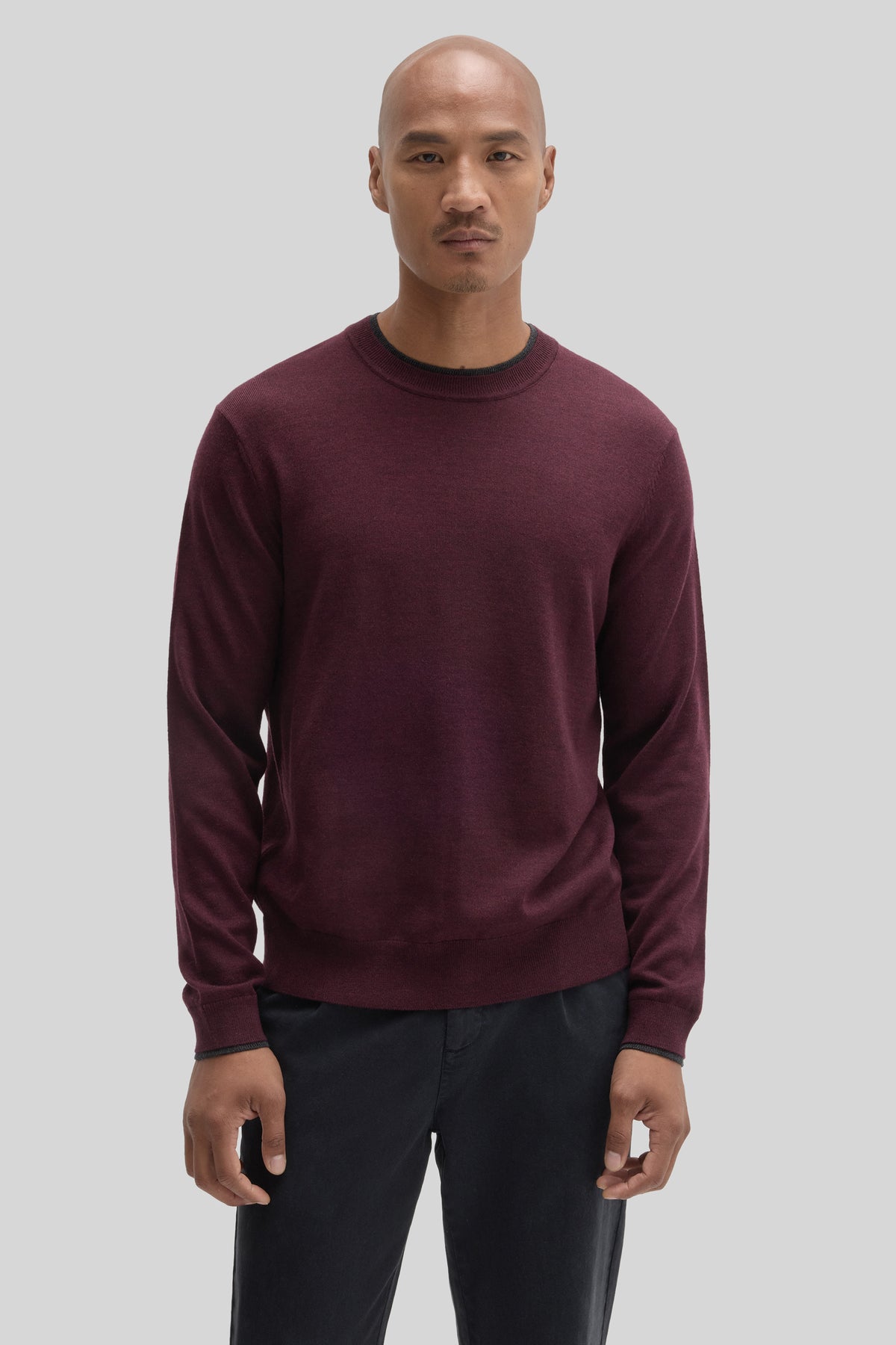 Burgundy crewneck sweater with ribbed trim, worn with dark trousers.
