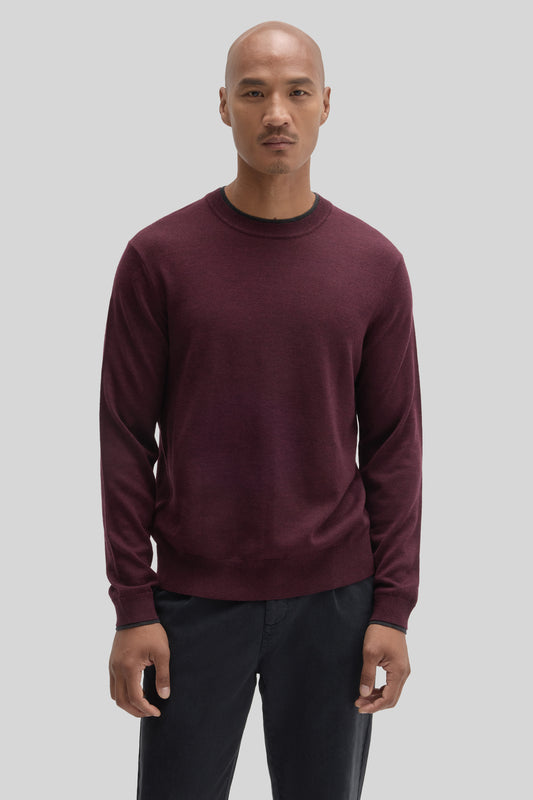 Burgundy crewneck sweater with ribbed trim, worn with dark trousers.