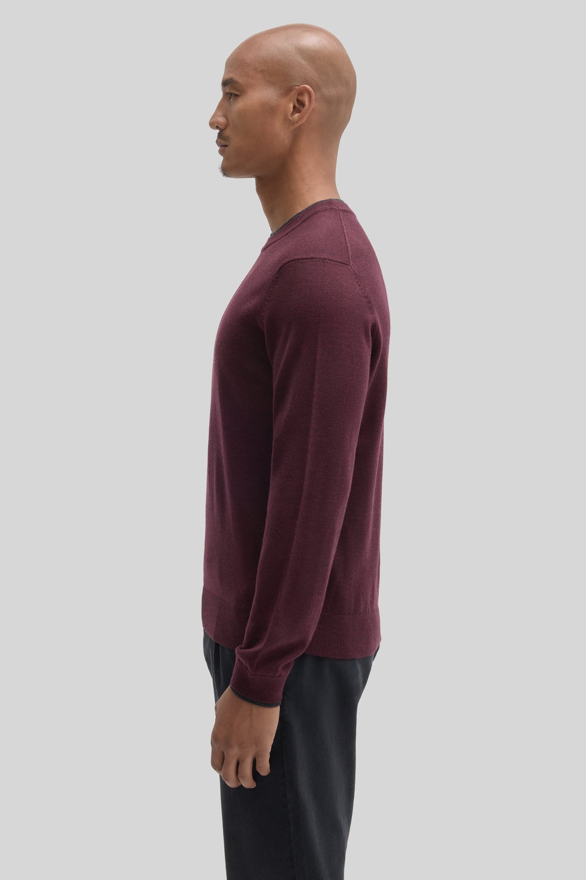 Burgundy crewneck sweater with long sleeves worn with black pants, shown in profile view.