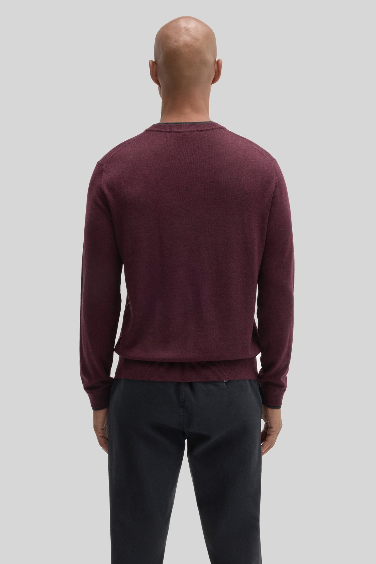 Man wearing burgundy crewneck sweater with long sleeves and ribbed trim, paired with dark pants, shown from back view.