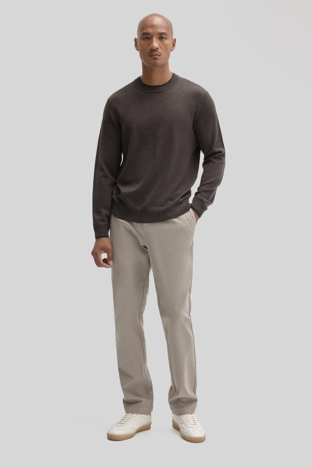 Man wearing charcoal crewneck sweater with beige pants and white sneakers.