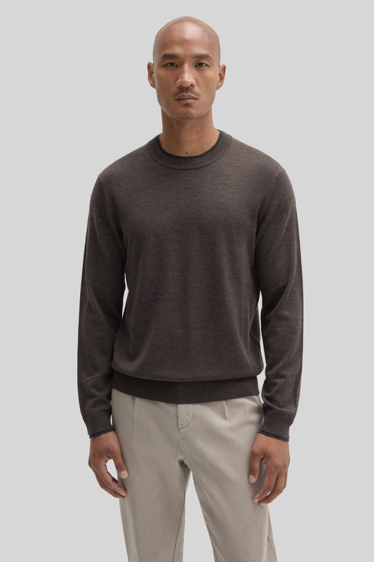 Man wearing dark gray crewneck sweater with long sleeves and ribbed trim, paired with beige pants.