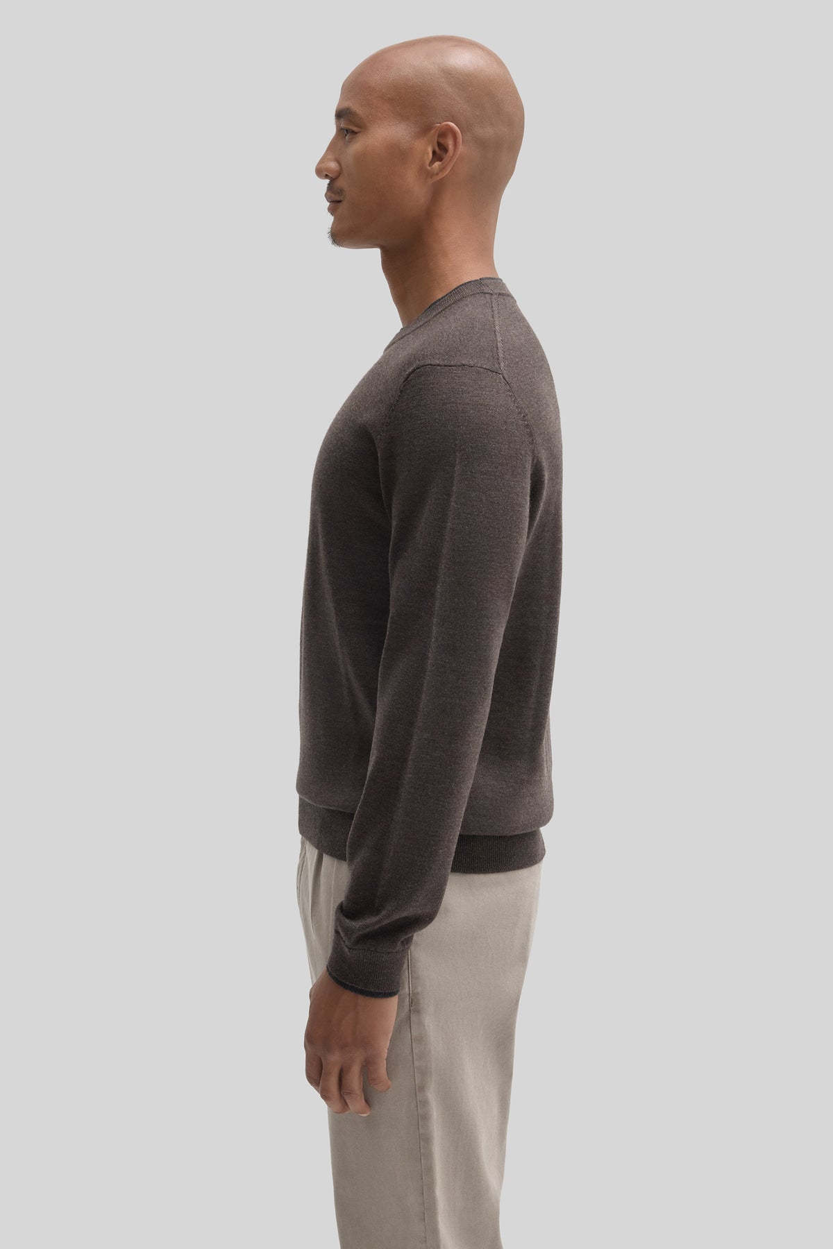 Charcoal crewneck sweater with ribbed cuffs and hem worn with beige trousers, shown from the side.