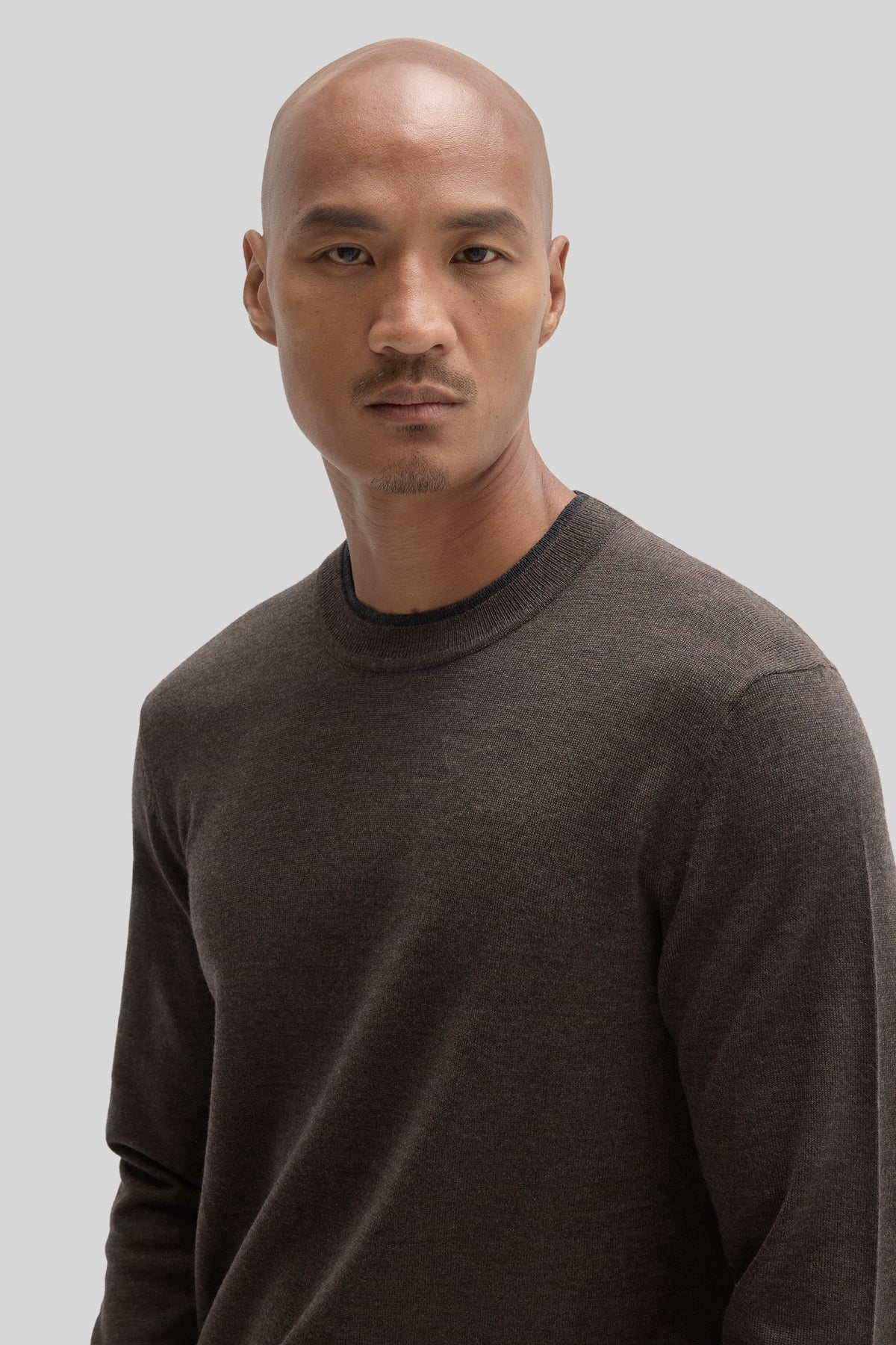 Charcoal crewneck sweater with ribbed neckline worn by man against neutral background.