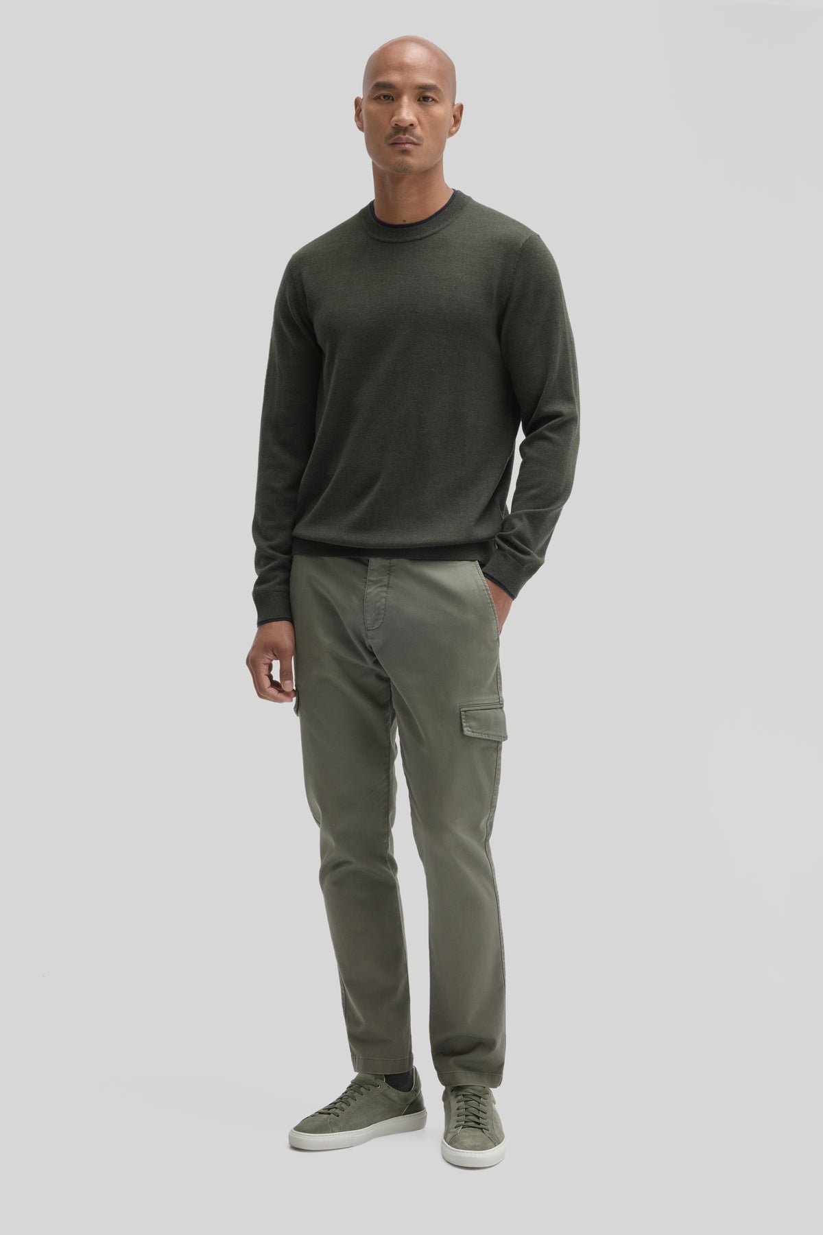 Man wearing dark olive crewneck sweater with long sleeves paired with sage cargo pants and olive sneakers.