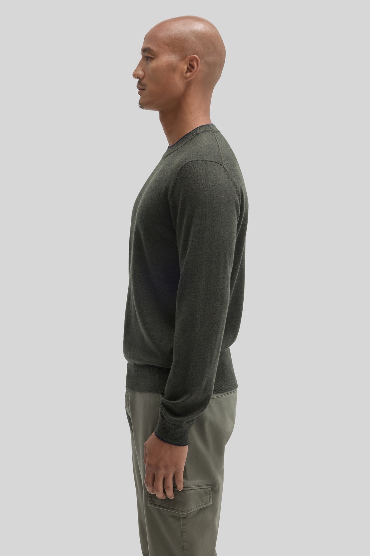 Man wearing olive green crewneck sweater with long sleeves, shown from side profile.