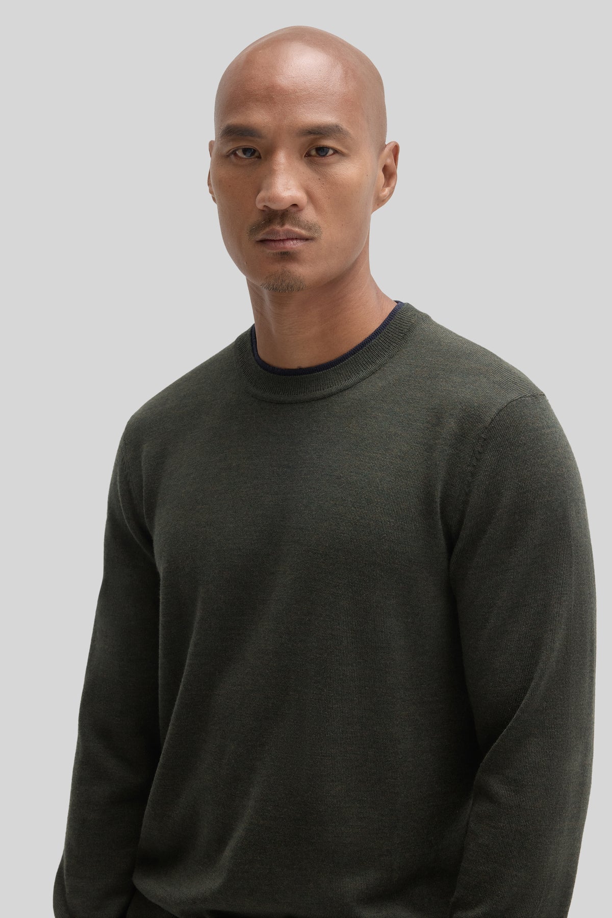 Man wearing olive green crewneck sweater with ribbed collar and cuffs.