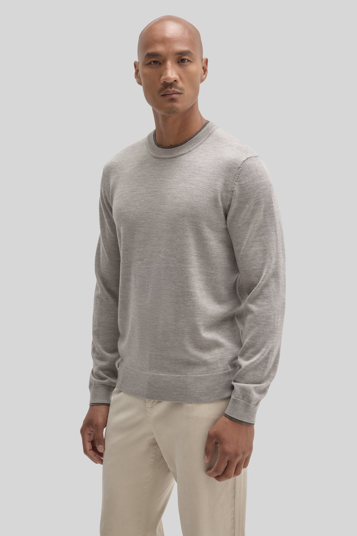 Man wearing light gray crewneck sweater with long sleeves and ribbed cuffs, paired with cream pants.
