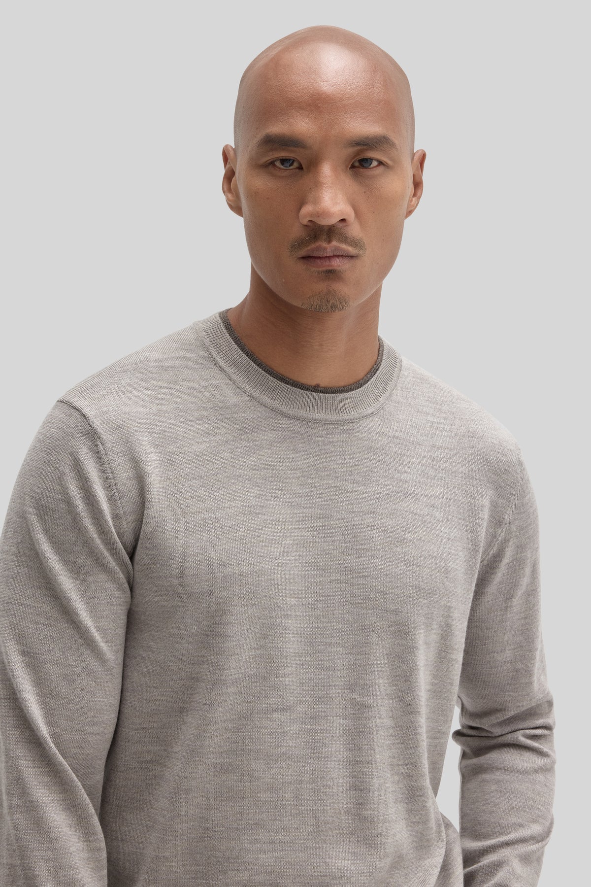Beige crewneck sweater with ribbed trim worn by a man against a neutral background.