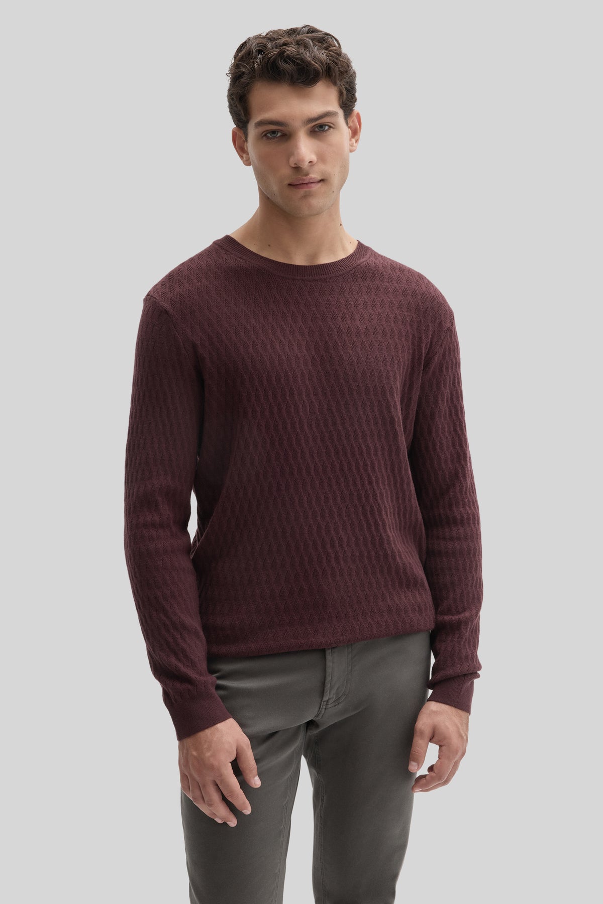 Man wearing burgundy crewneck sweater with textured knit pattern and gray pants.