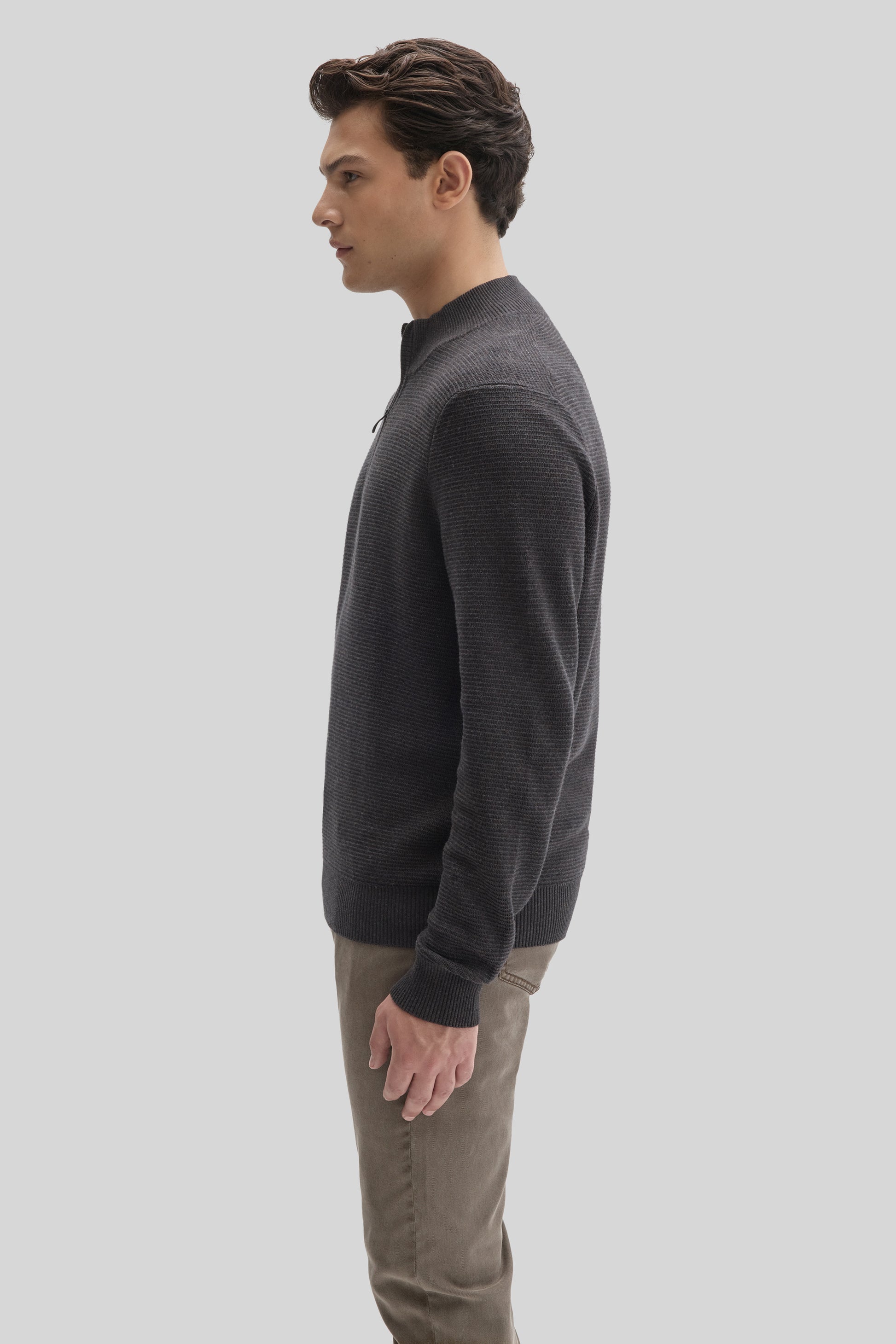 Man wearing charcoal quarter zip sweater with ribbed texture and tan pants, shown in side profile.