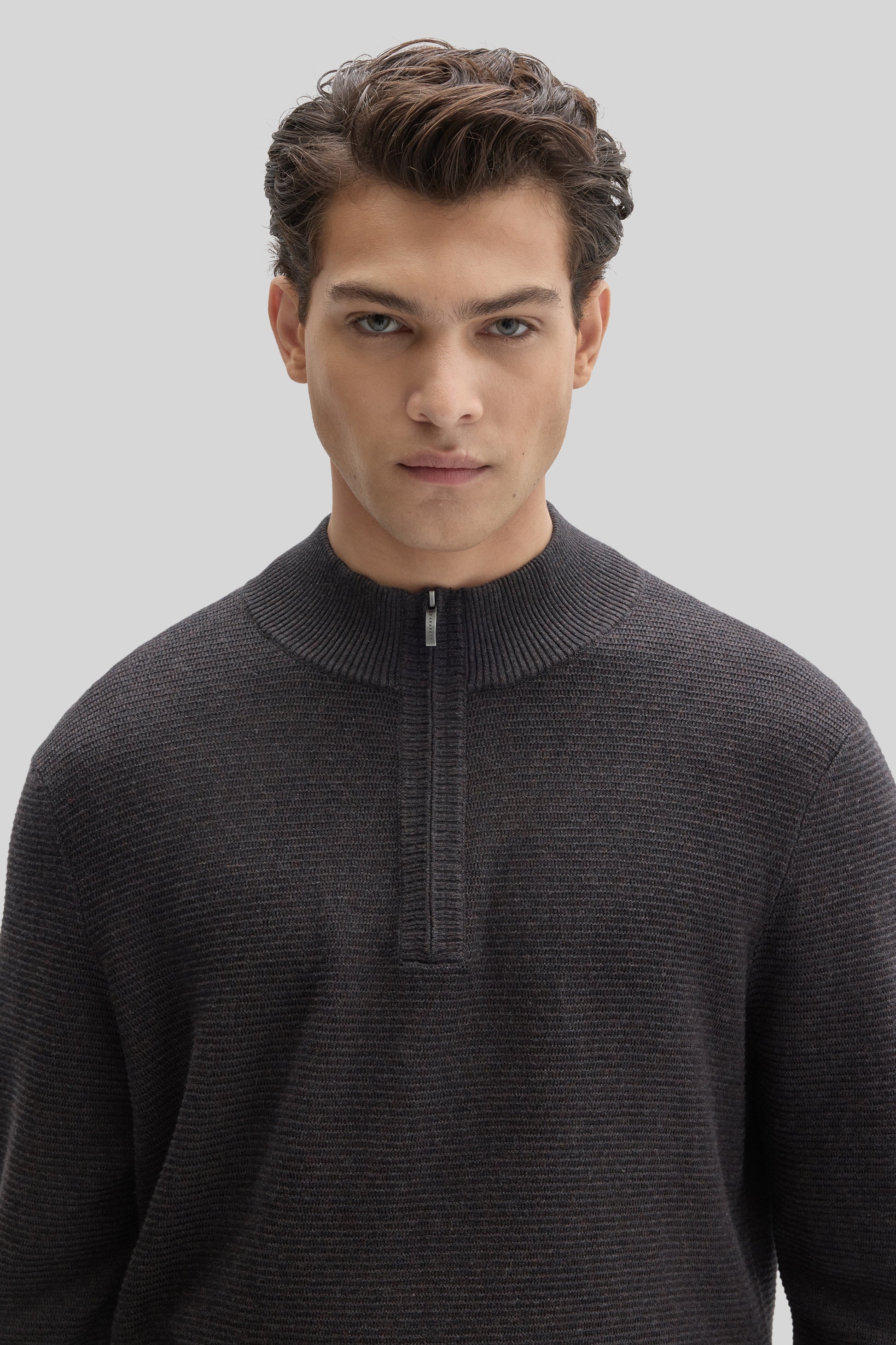 Charcoal gray quarter zip sweater with ribbed knit texture worn by a man against a neutral background.