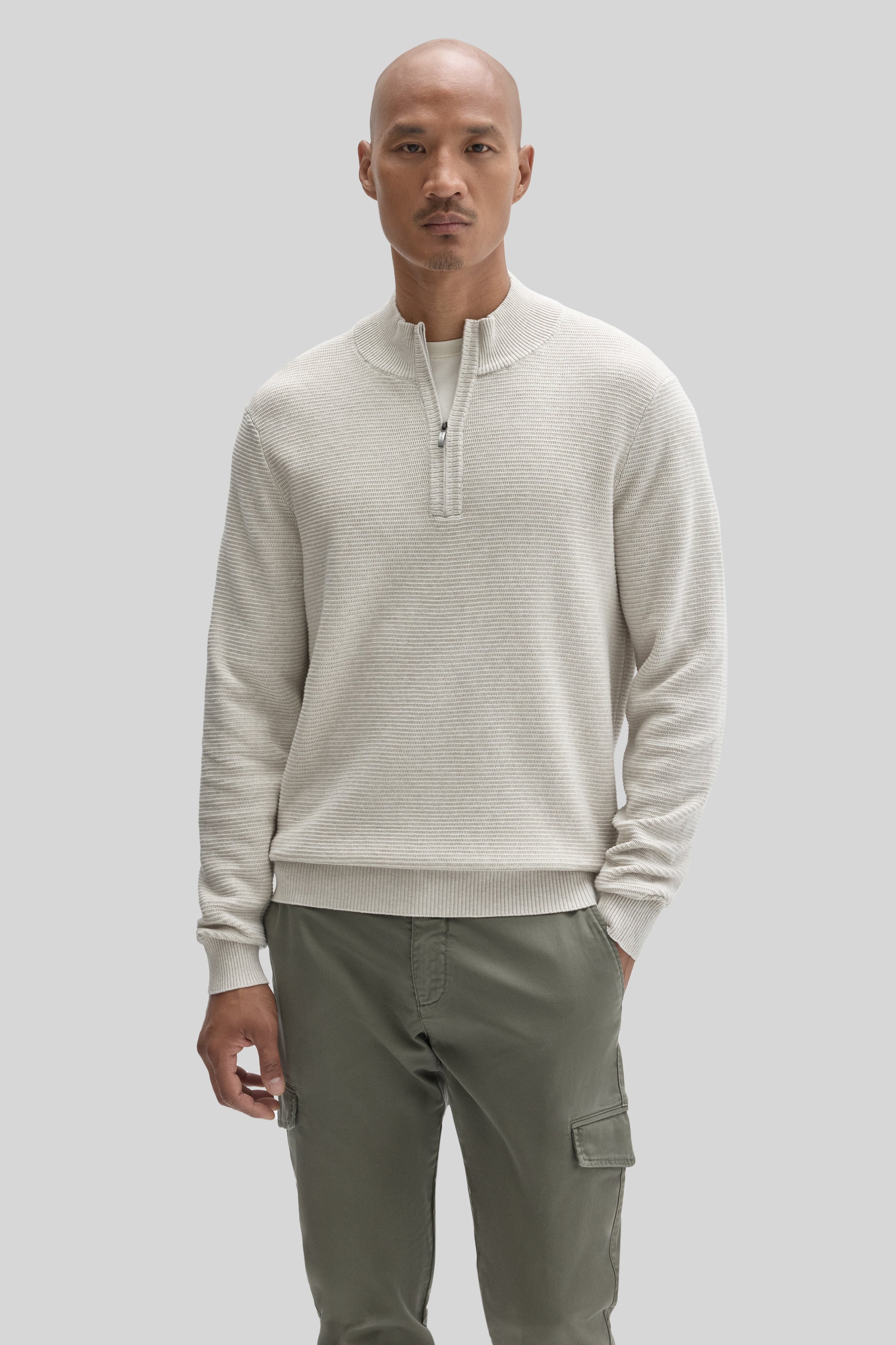 Man wearing cream quarter-zip sweater with ribbed texture and olive cargo pants with side pockets.
