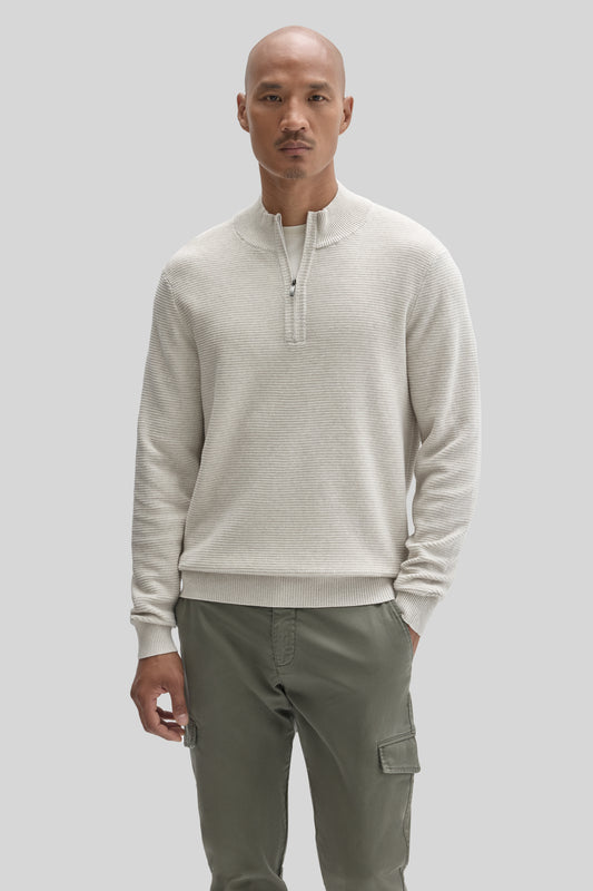 Man wearing cream quarter-zip sweater with ribbed texture and olive cargo pants with side pockets.
