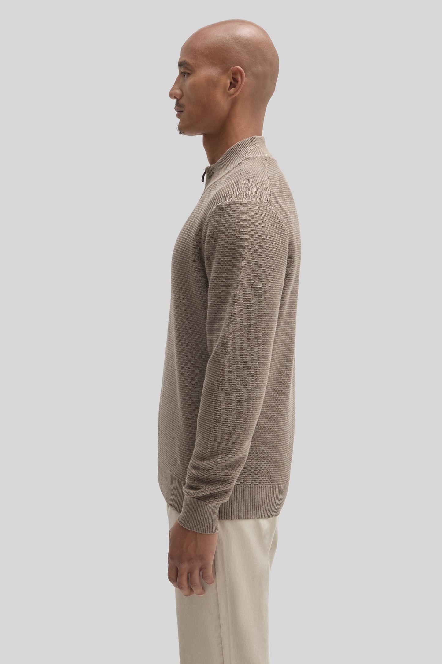 Beige ribbed quarter-zip sweater with mock neckline worn by a man in profile view.