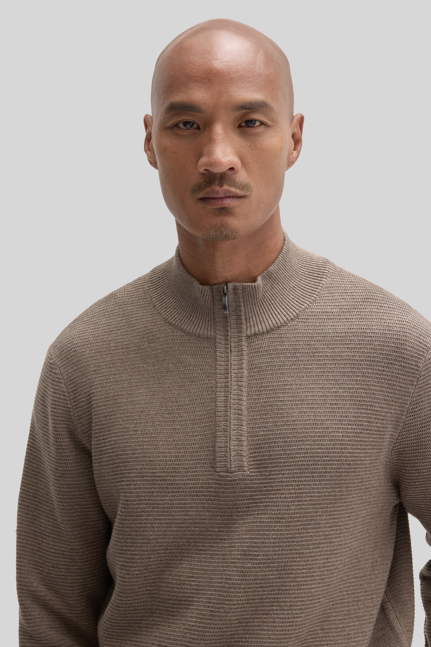Beige quarter zip sweater with ribbed texture worn by a man against a neutral background.