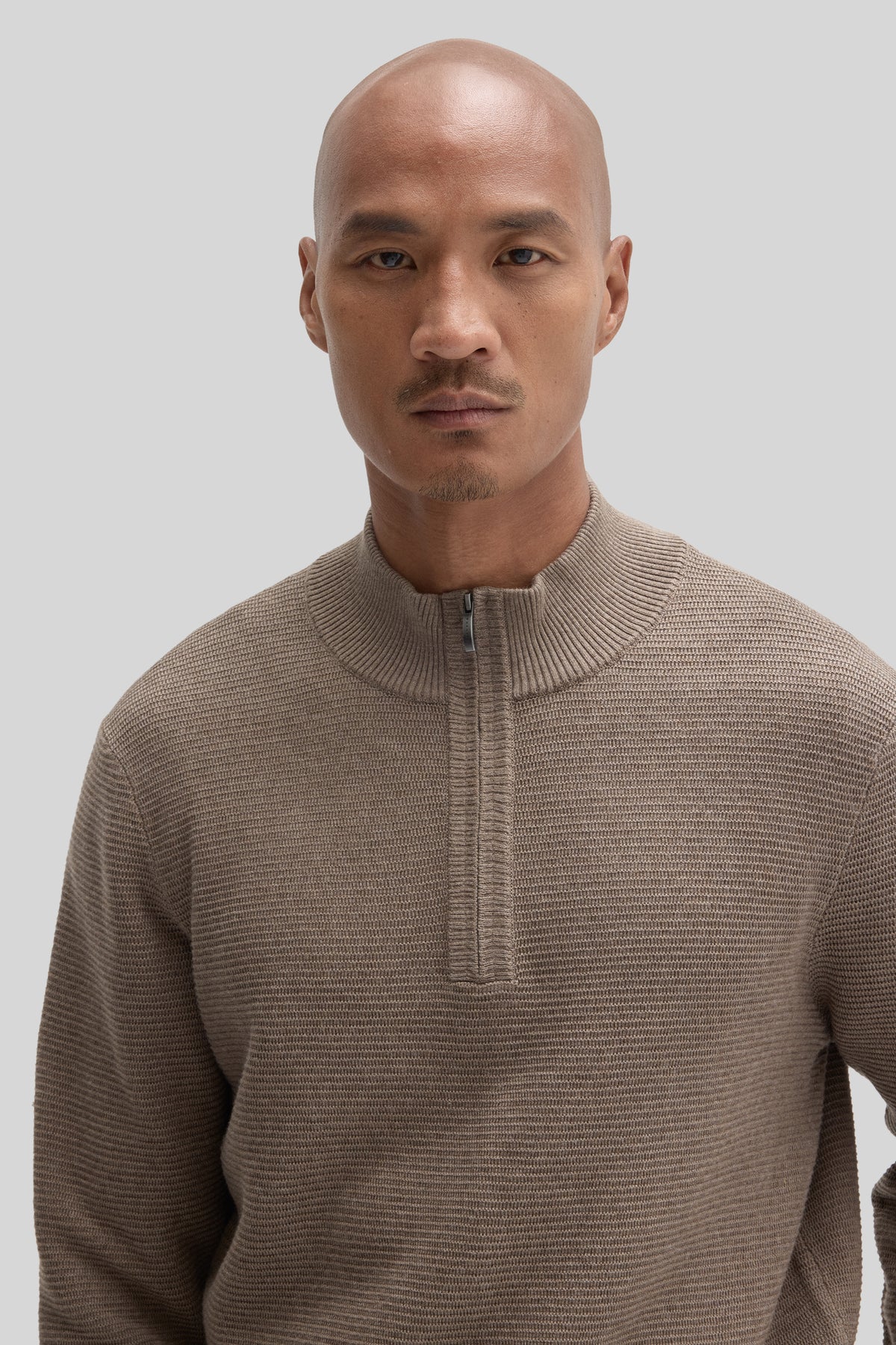 Beige quarter zip sweater with ribbed texture worn by a man against a neutral background.