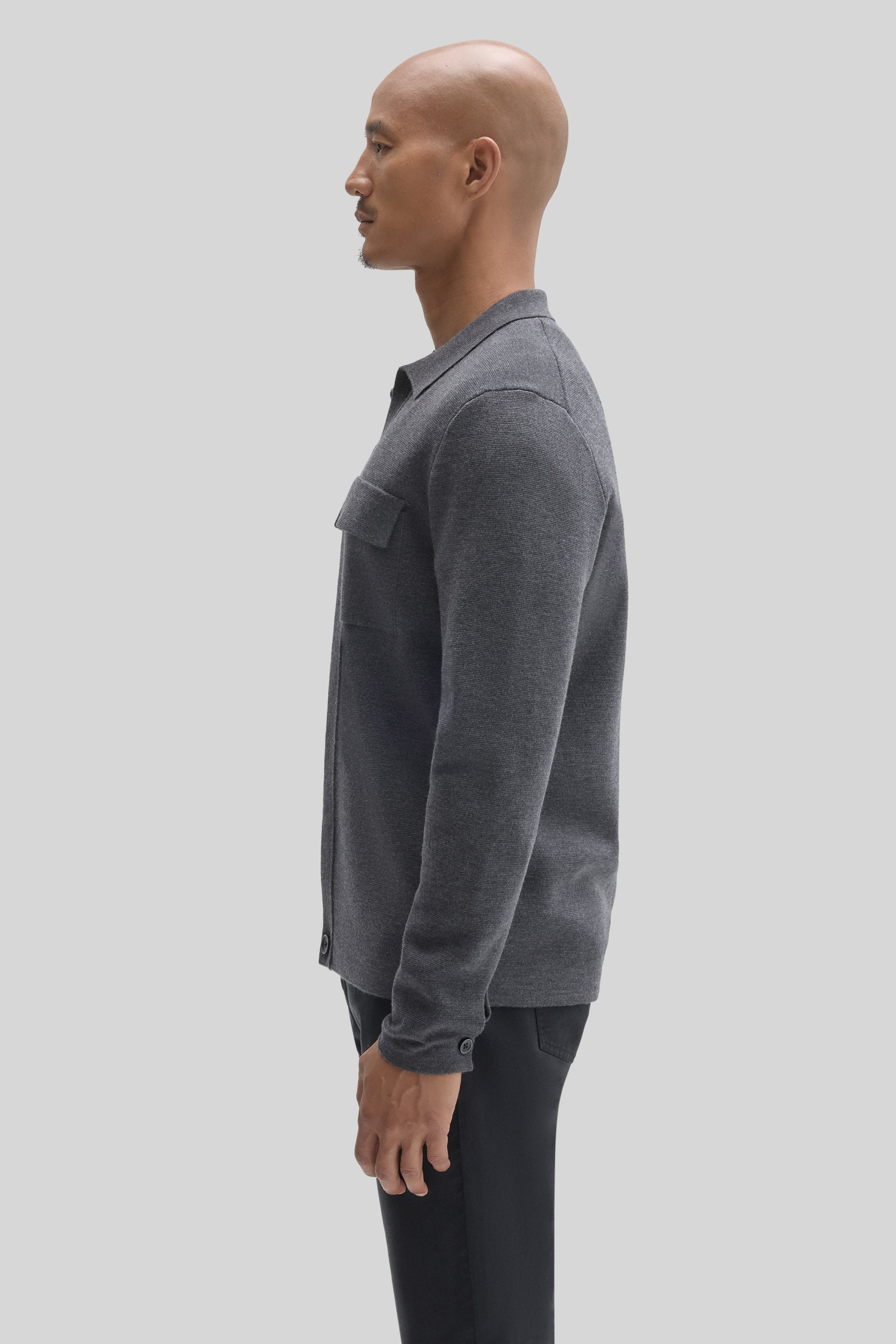 Charcoal gray buttoned cardigan with chest pocket, worn unbuttoned over black pants.