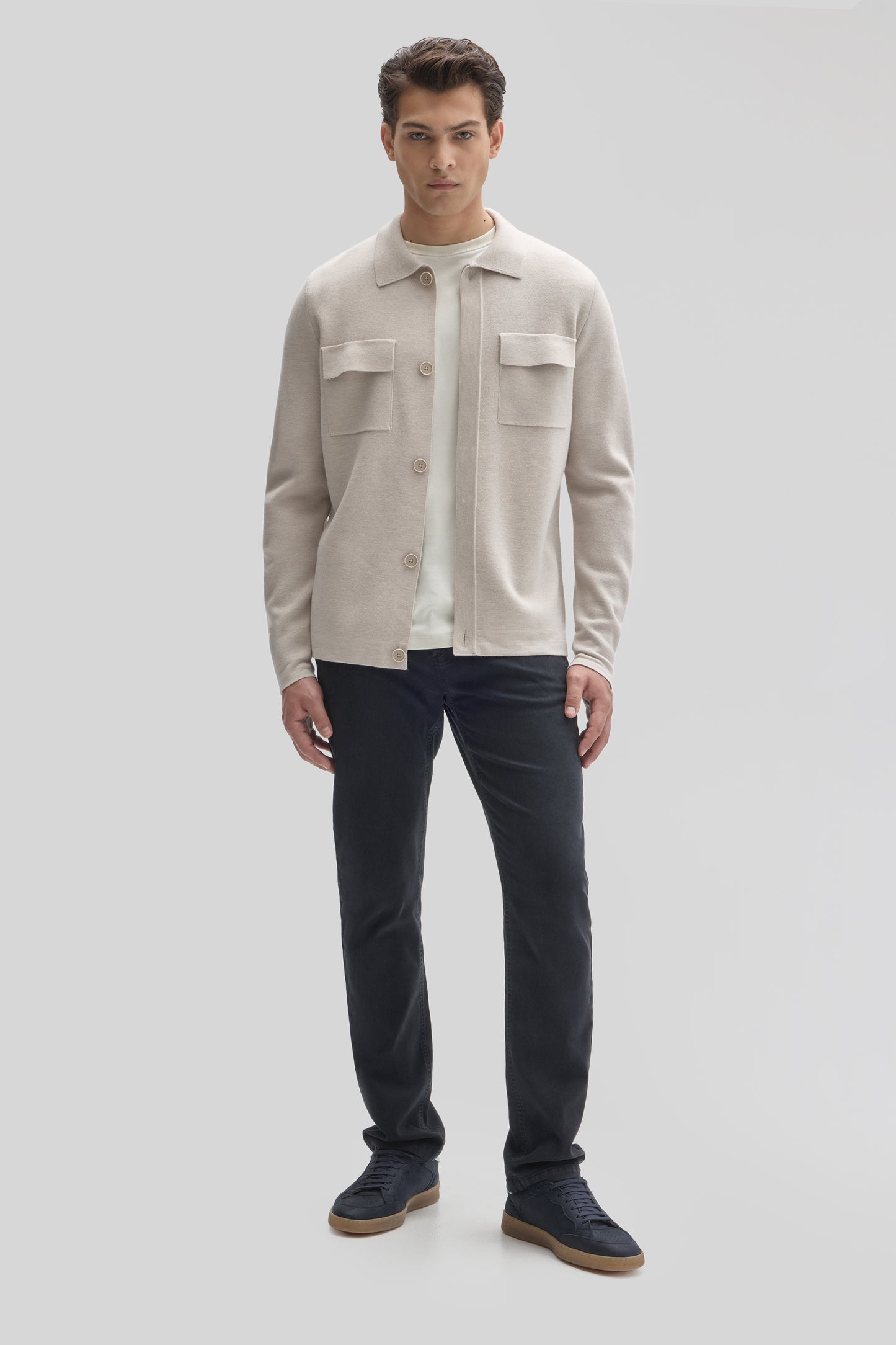 Beige buttoned cardigan with chest pockets worn over white undershirt and dark navy pants.